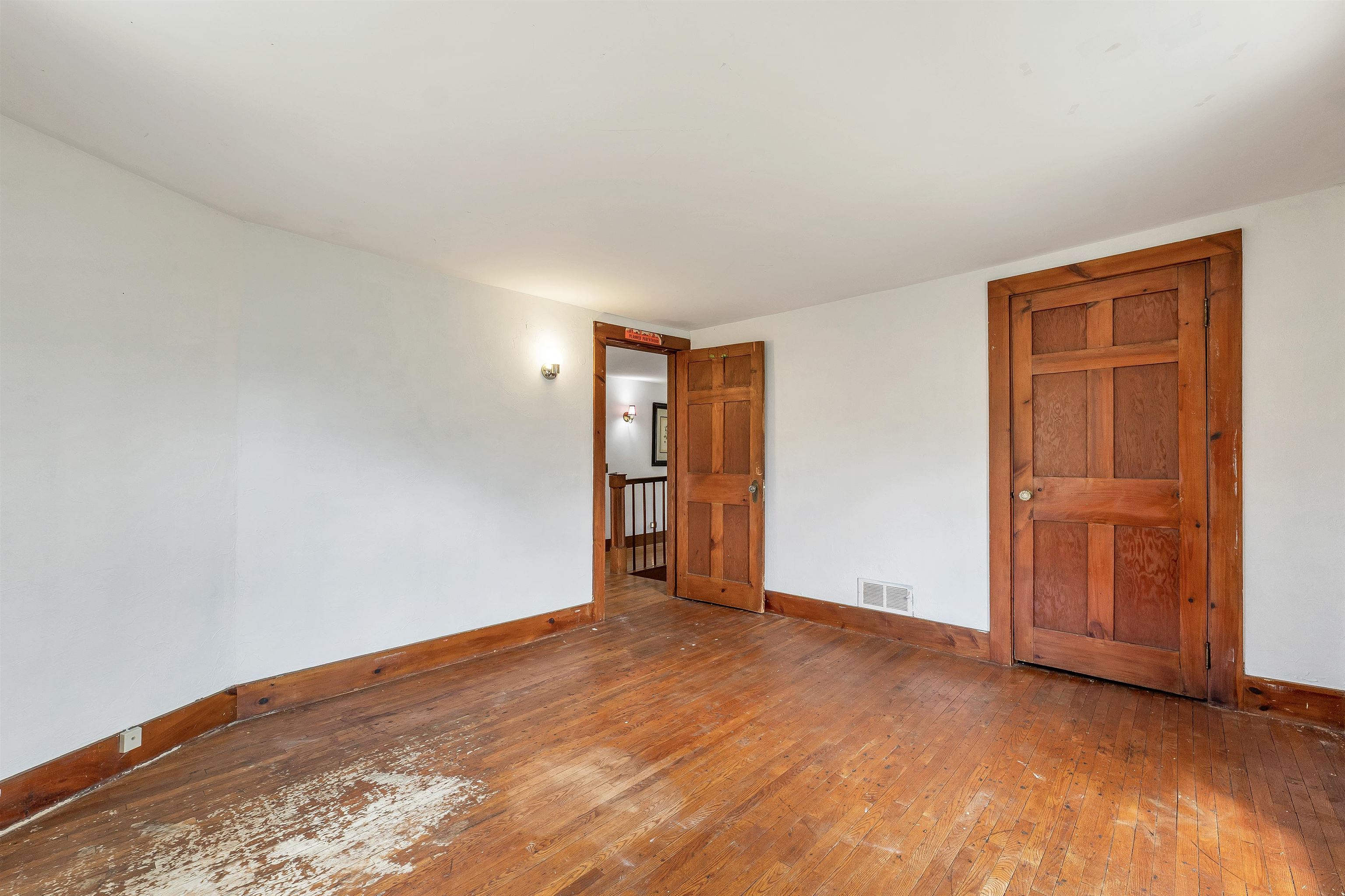 Empty room with worn hardwood floors, white walls, and reddish-brown wooden doors and trim.