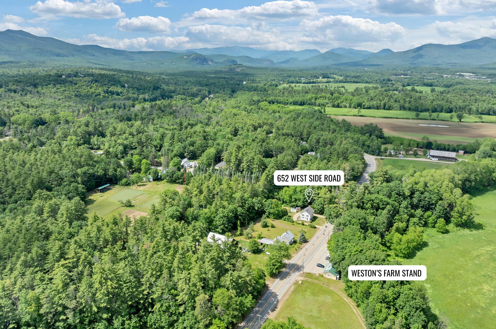 Aerial view of a white house amid woodland and fields, with the White Mountains in the distance.