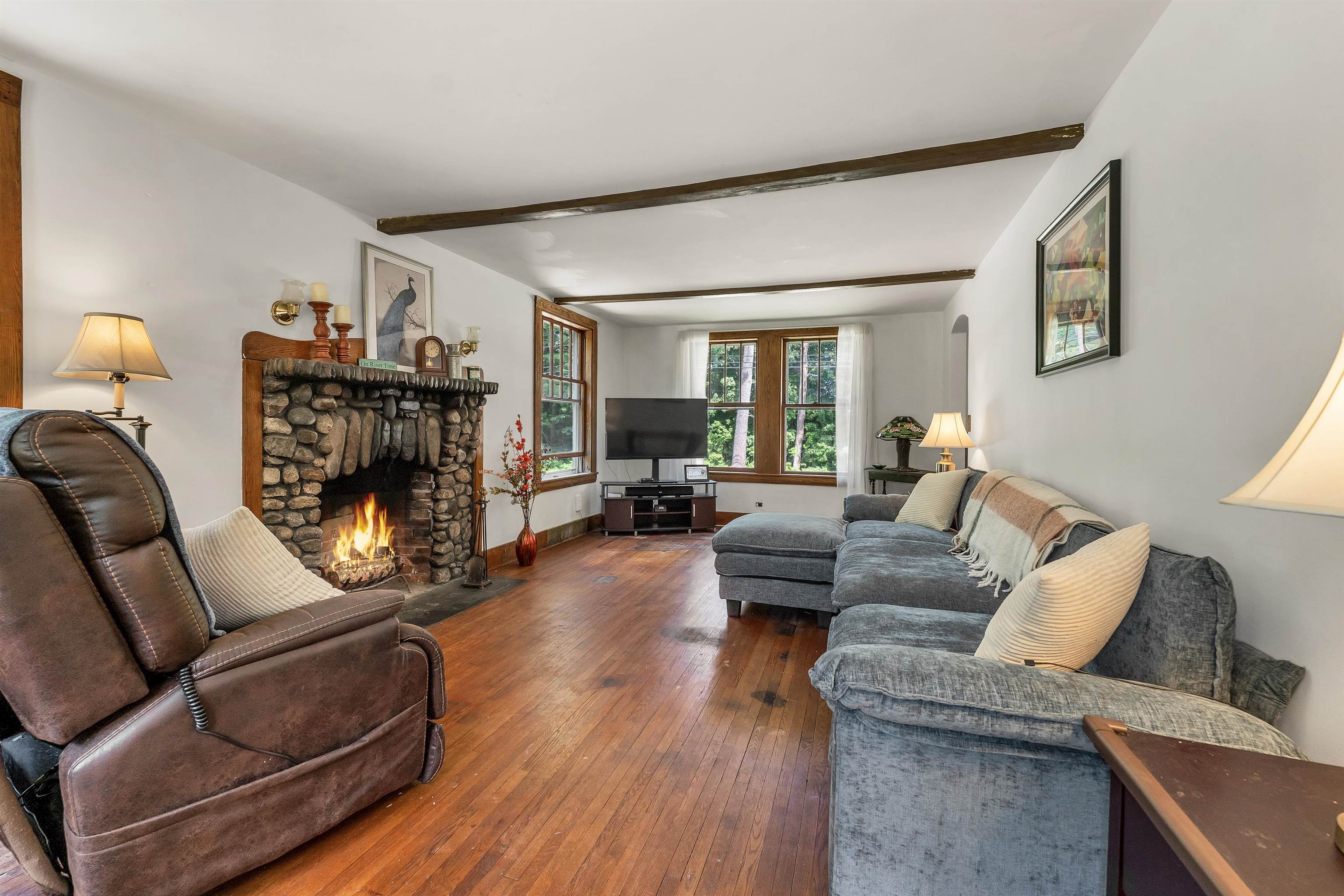 Living room with a stone fireplace, exposed beams, hardwood floors, and a gray sectional sofa.