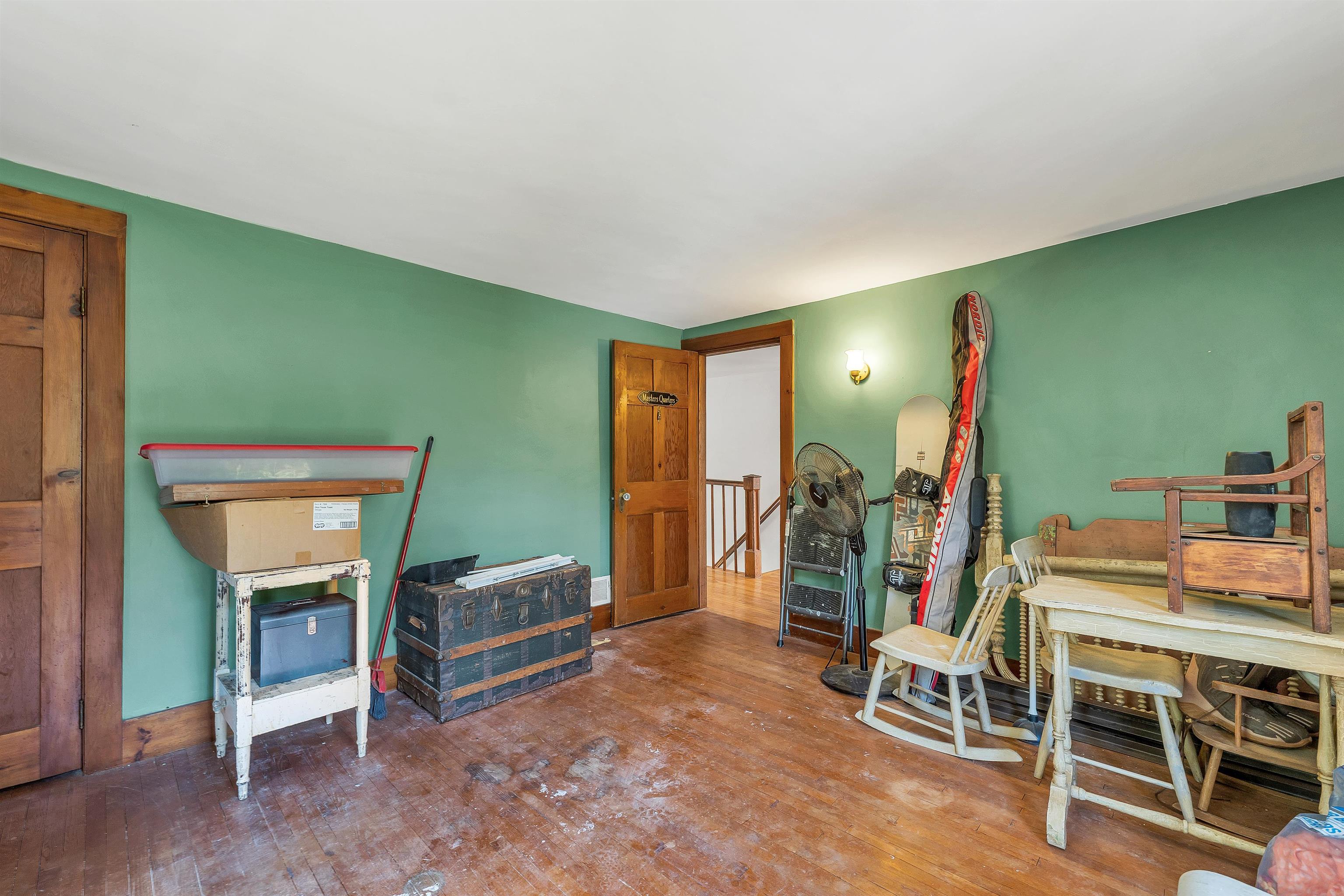 Storage room with green walls, a worn wood floor, a trunk, stacked furniture, and winter sports equipment.
