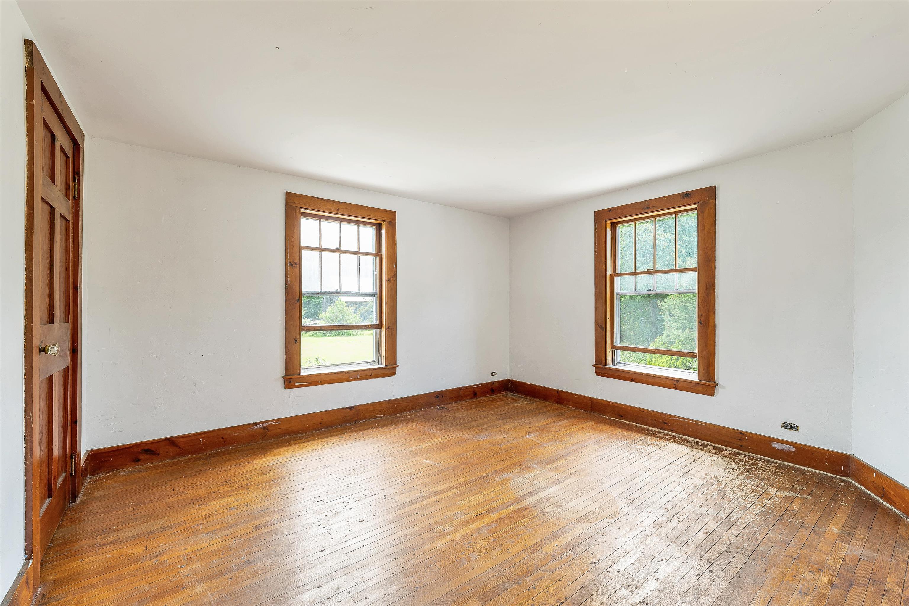 Empty room with worn hardwood floors and two wood-trimmed windows.