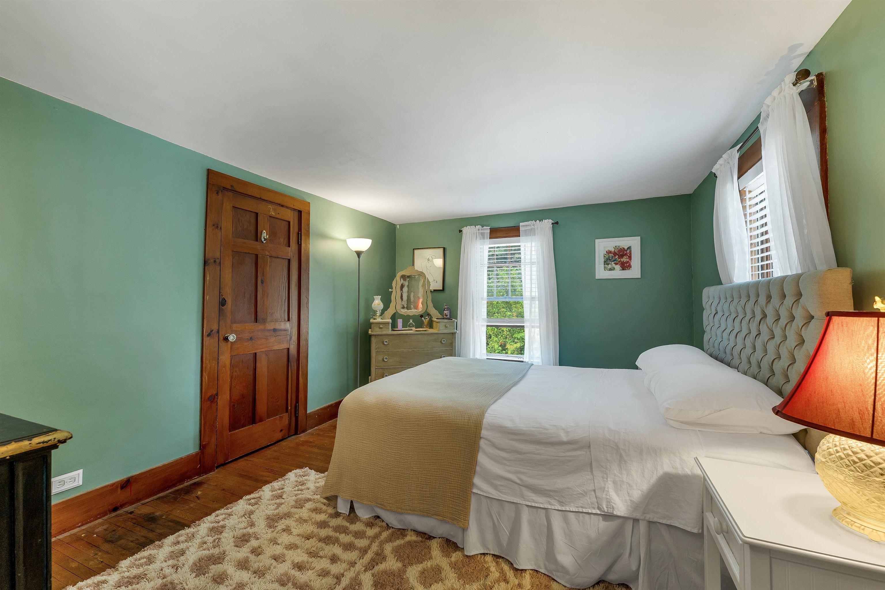 Bedroom with green walls, a white bed, hardwood floors, and a vintage wooden door.