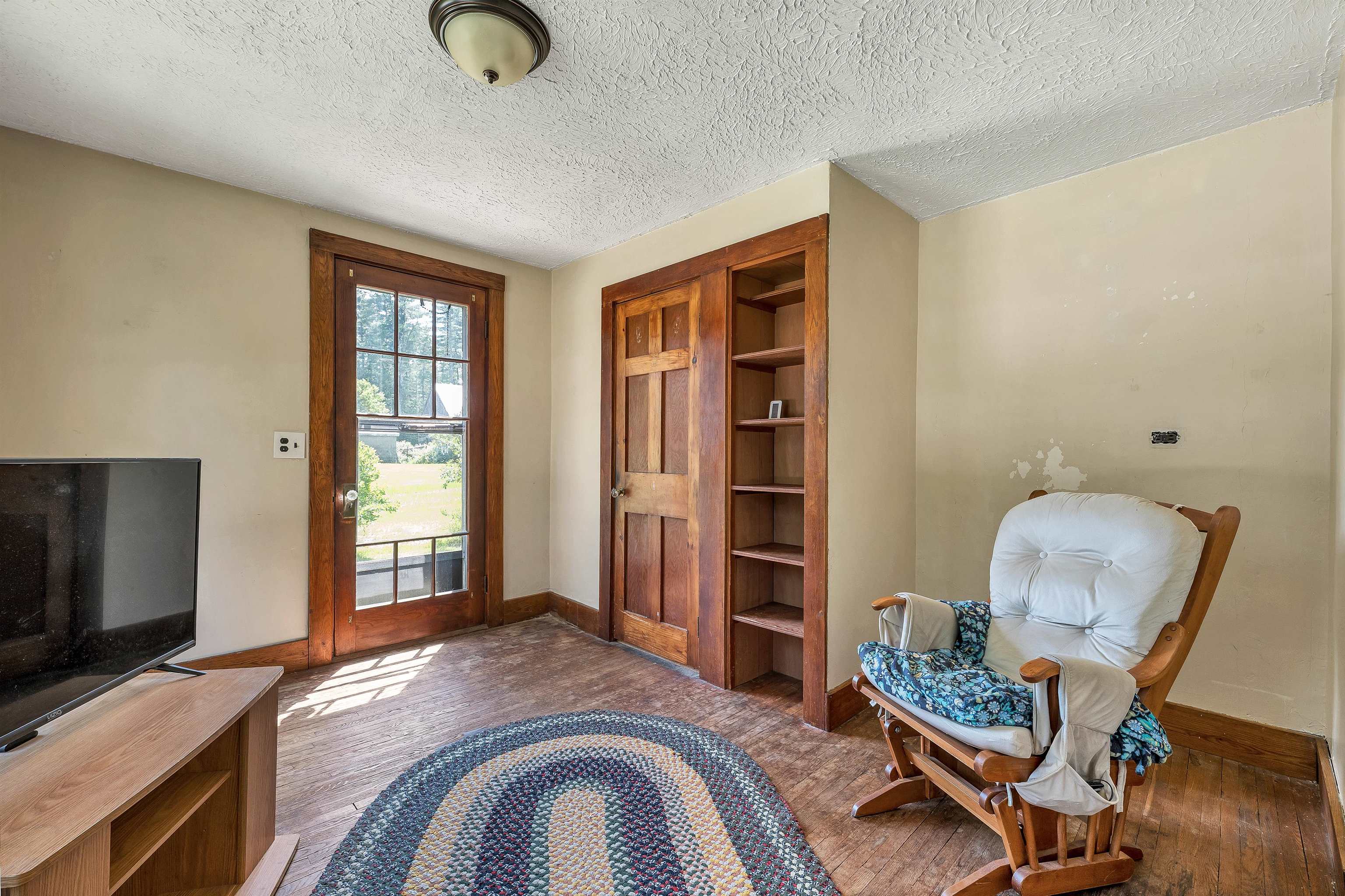 Living room with a glass-paneled door, built-in wooden shelves, and a cushioned rocking chair.