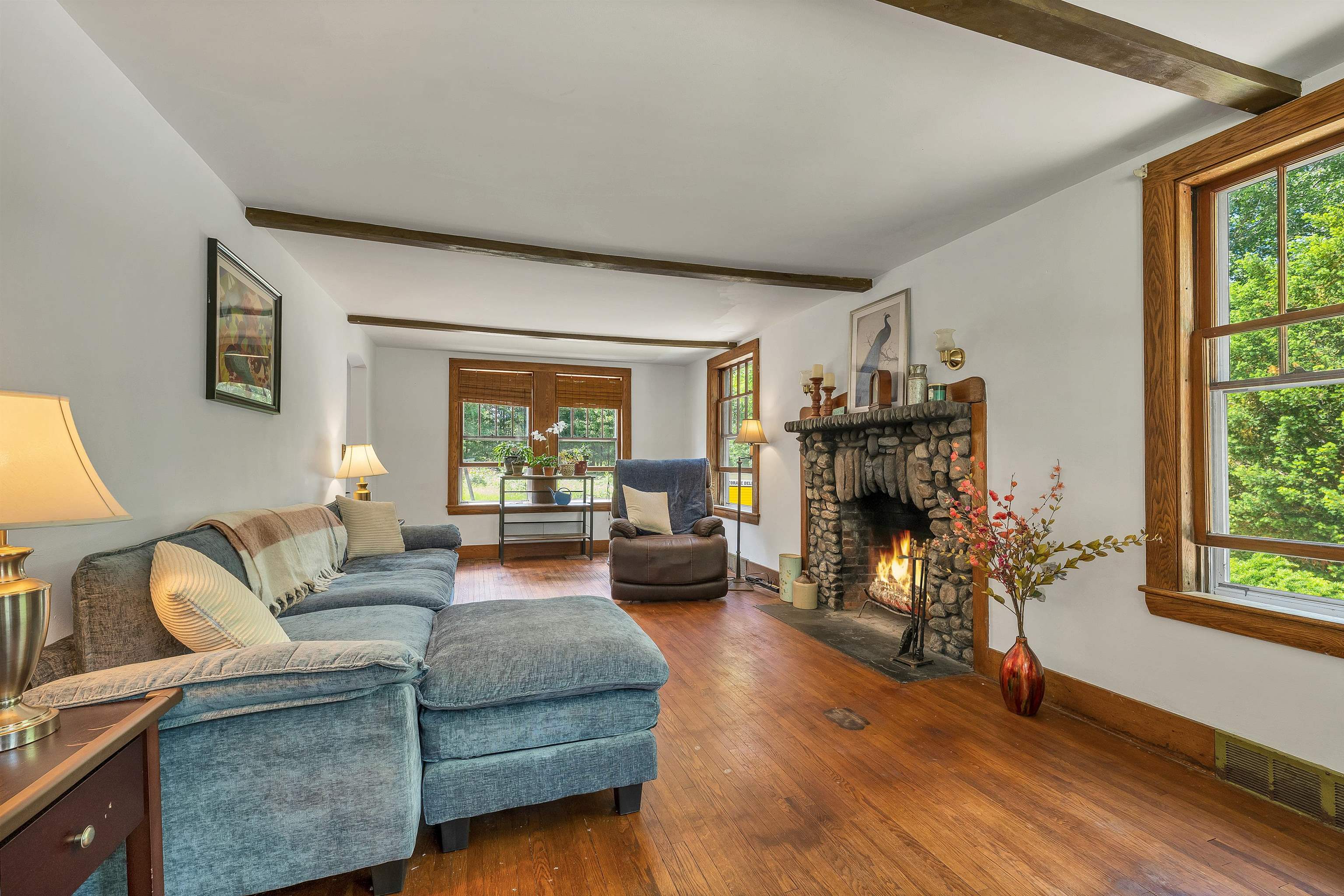 Living room with a blue sectional sofa, exposed beams, and a large stone fireplace.