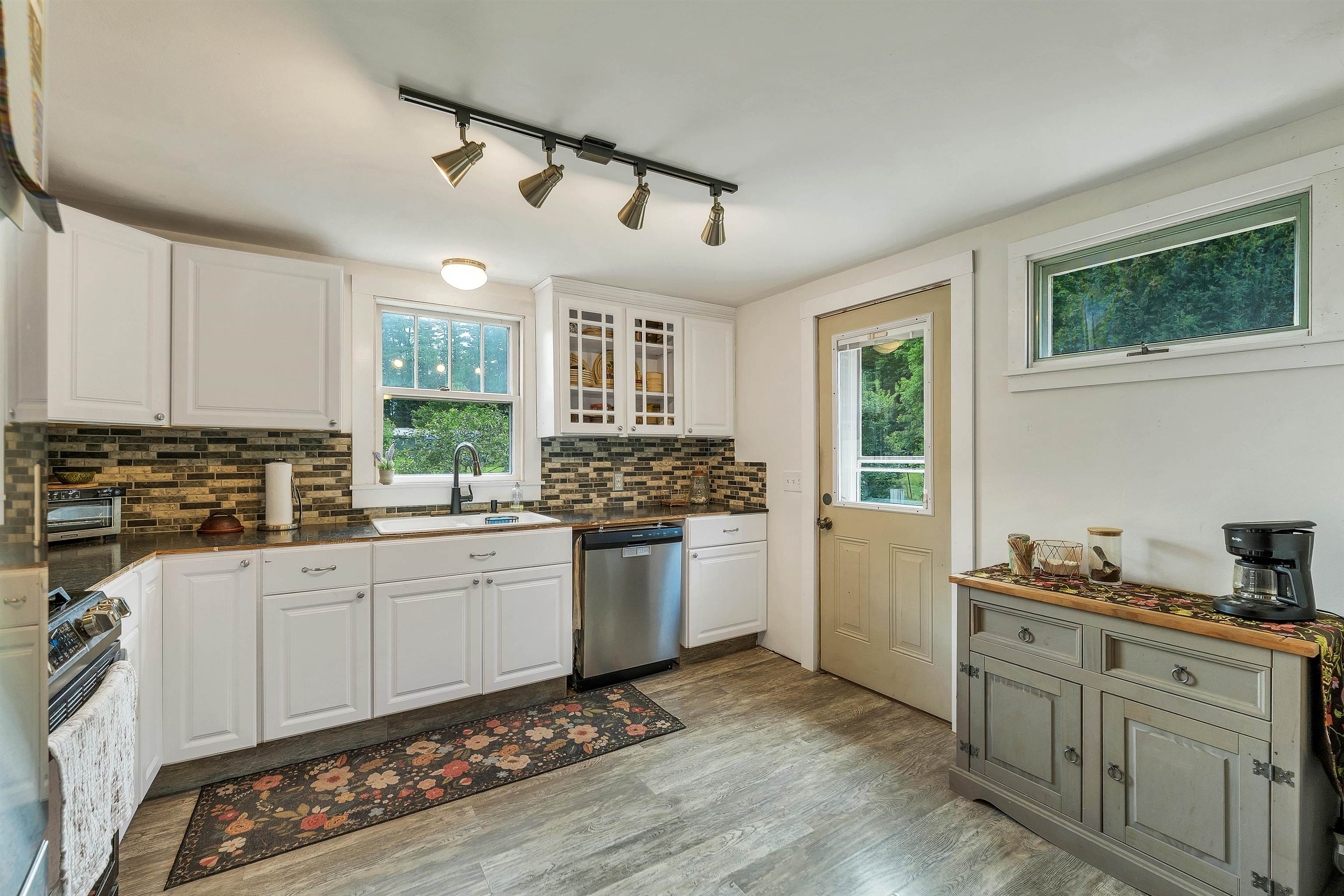 Kitchen with white cabinets, a multicolored tile backsplash, and a sink beneath a window.