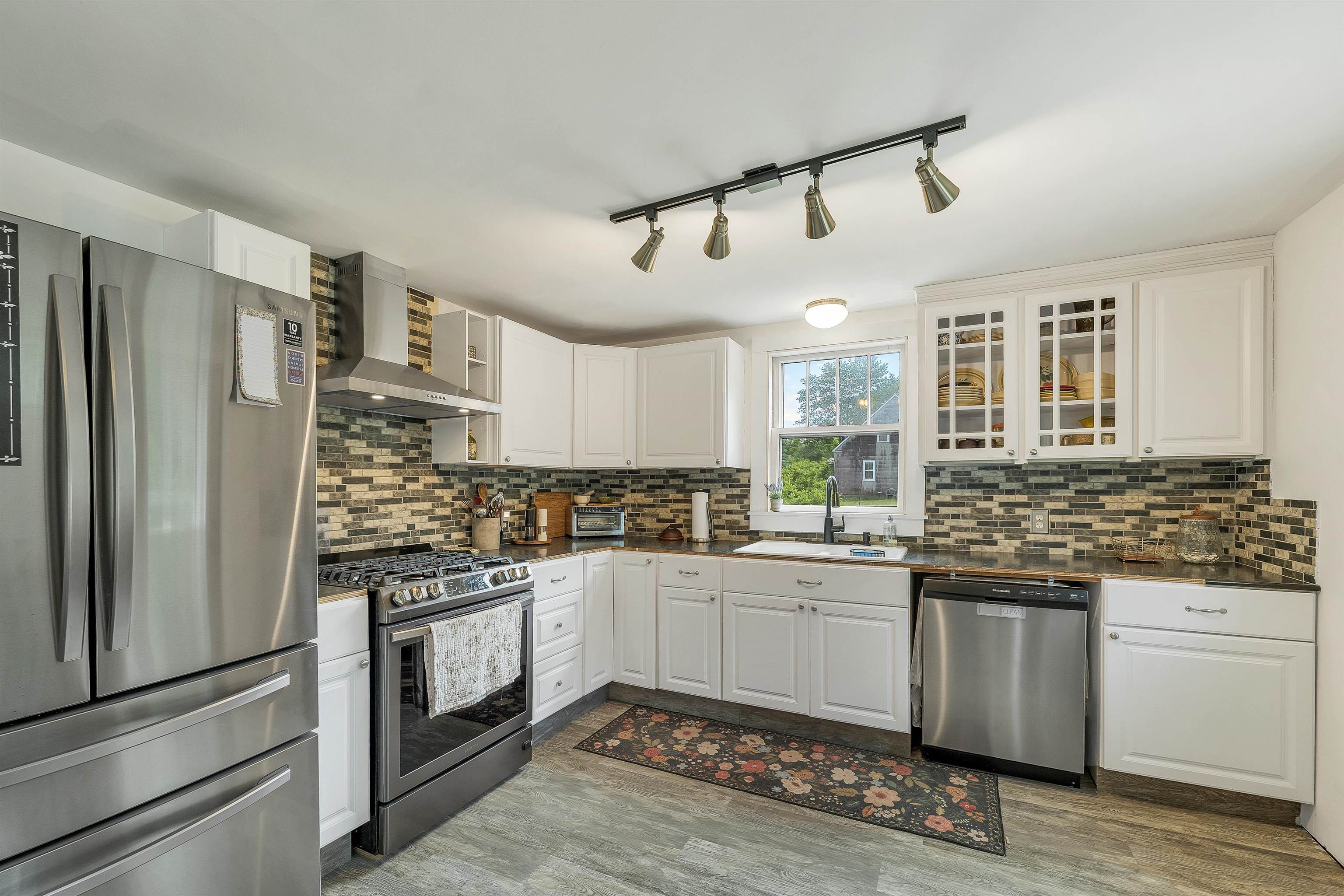 Kitchen with white cabinets, stainless steel appliances, and a multicolor brick-pattern backsplash.
