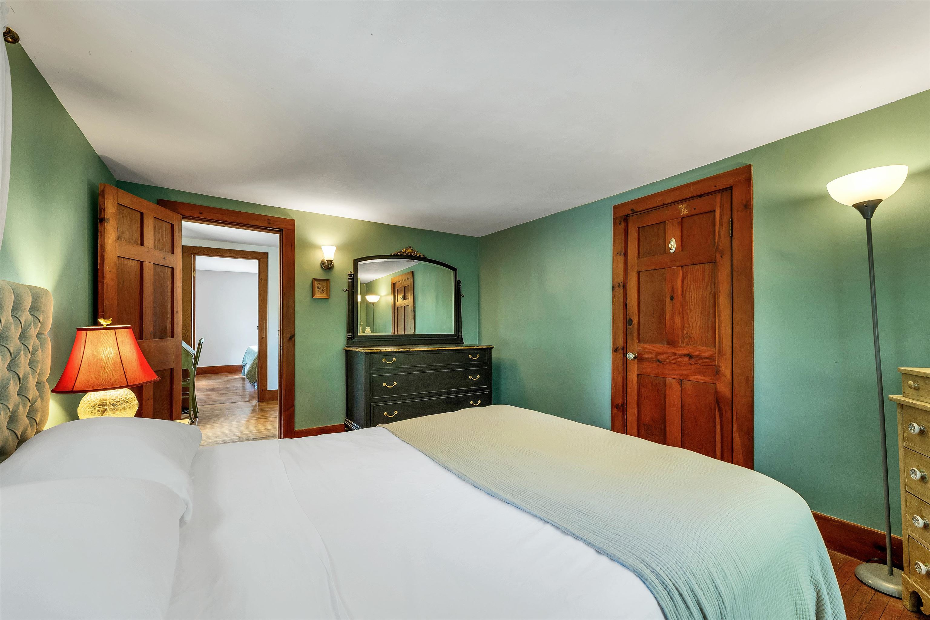 Bedroom with green walls, wood doors and trim, and a bed with a pale blue coverlet.