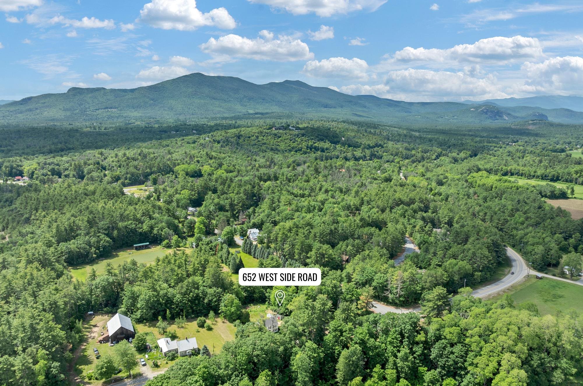 Aerial view of 652 West Side Road amid dense forest, with mountain ranges in the distance.
