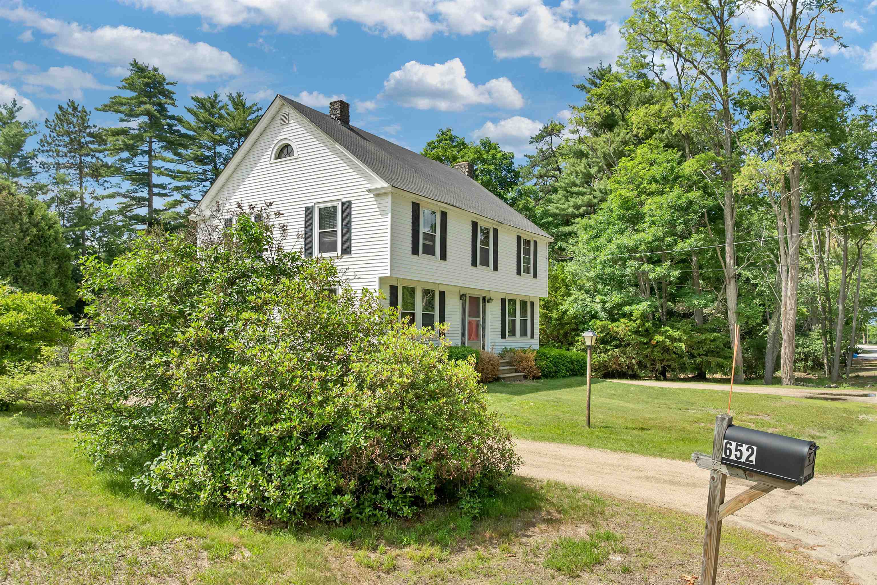 White two-story house with dark shutters, framed by mature trees; mailbox marked 652 beside the driveway.