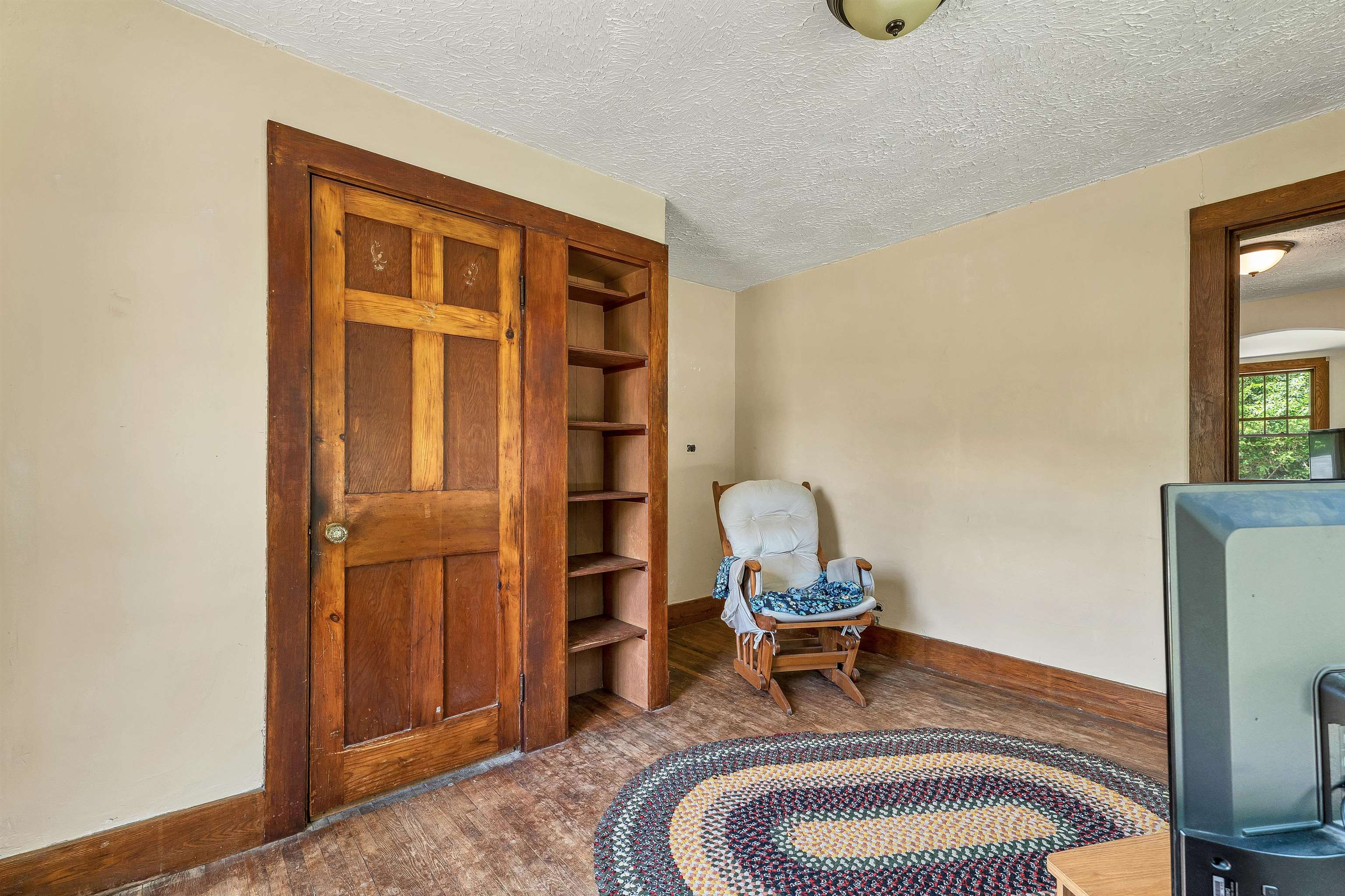 Room with built-in wooden shelves, a paneled door, rocking chair, and braided rug.