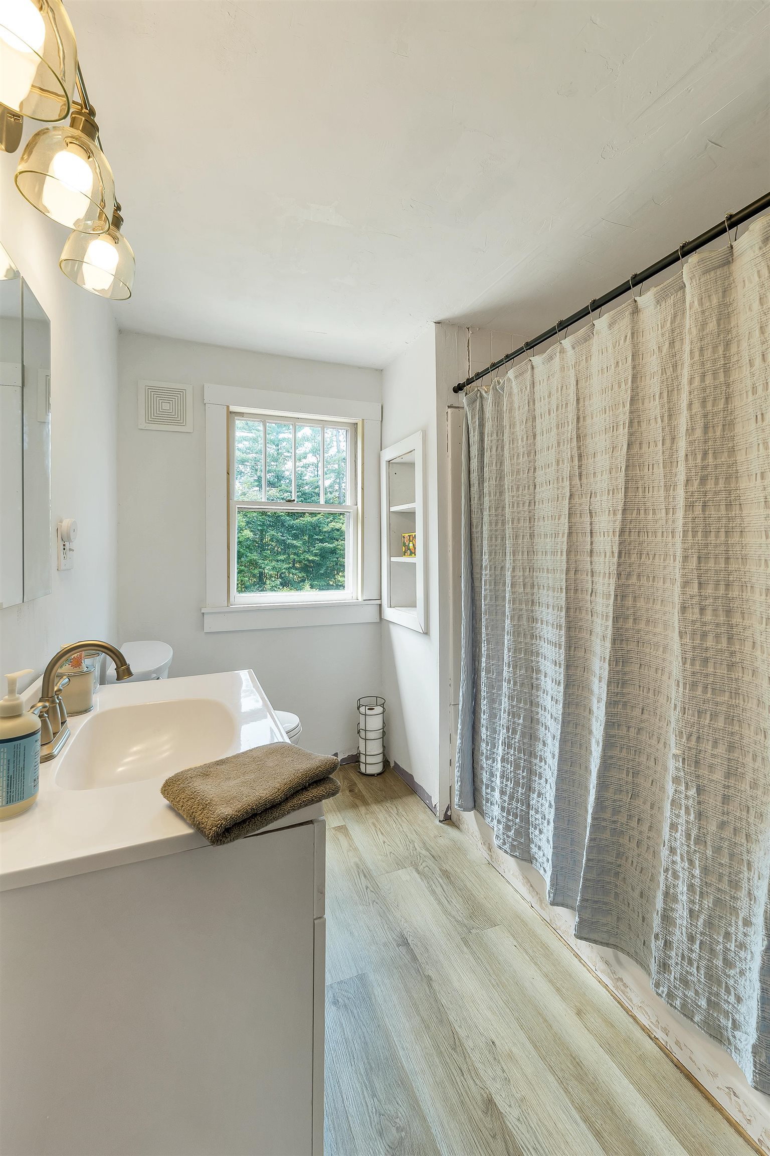 Bathroom with white vanity, brass fixtures, and a window beside a textured shower curtain.