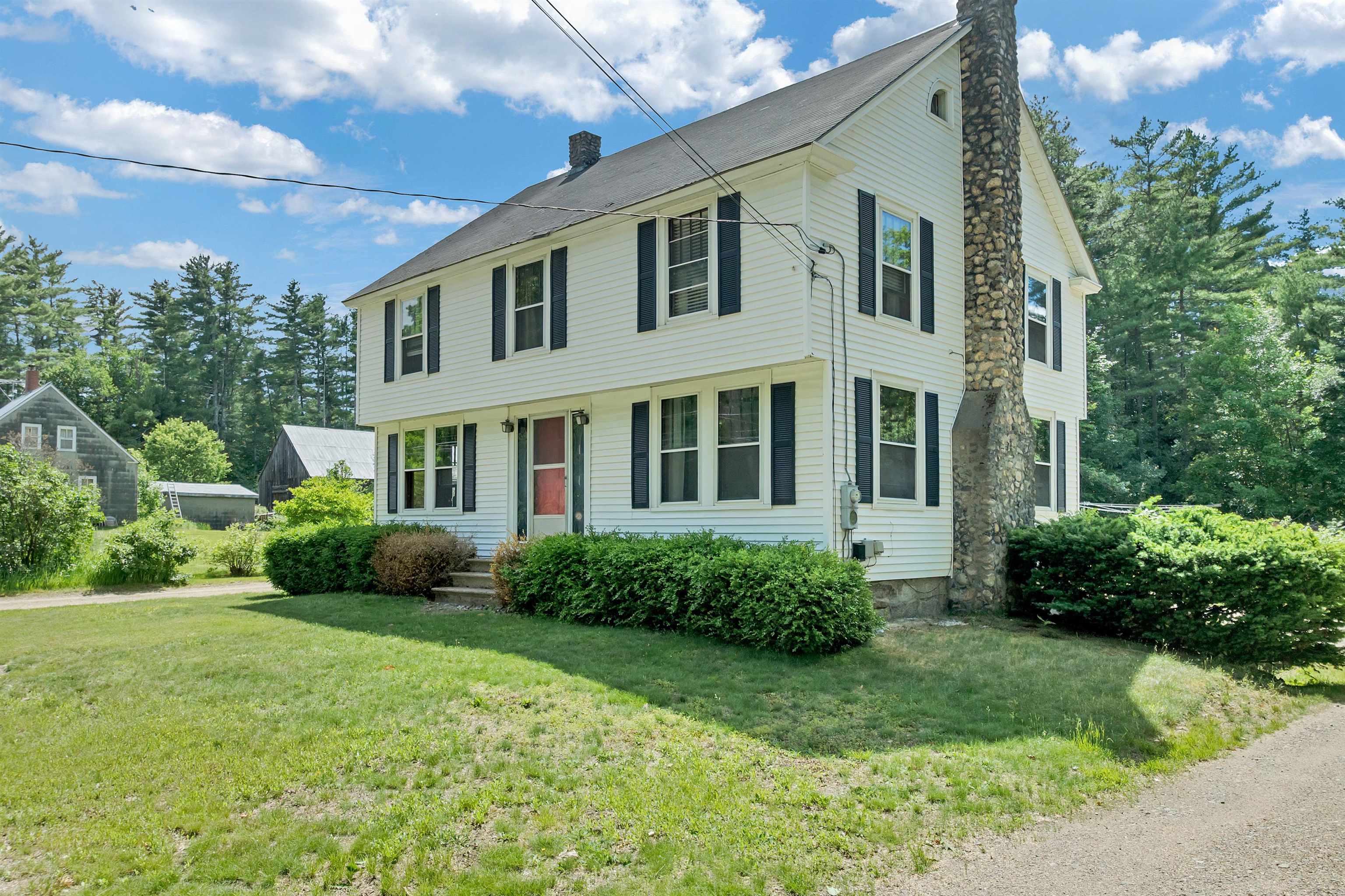 White two-story house with dark shutters, a red front door, and a tall stone chimney.