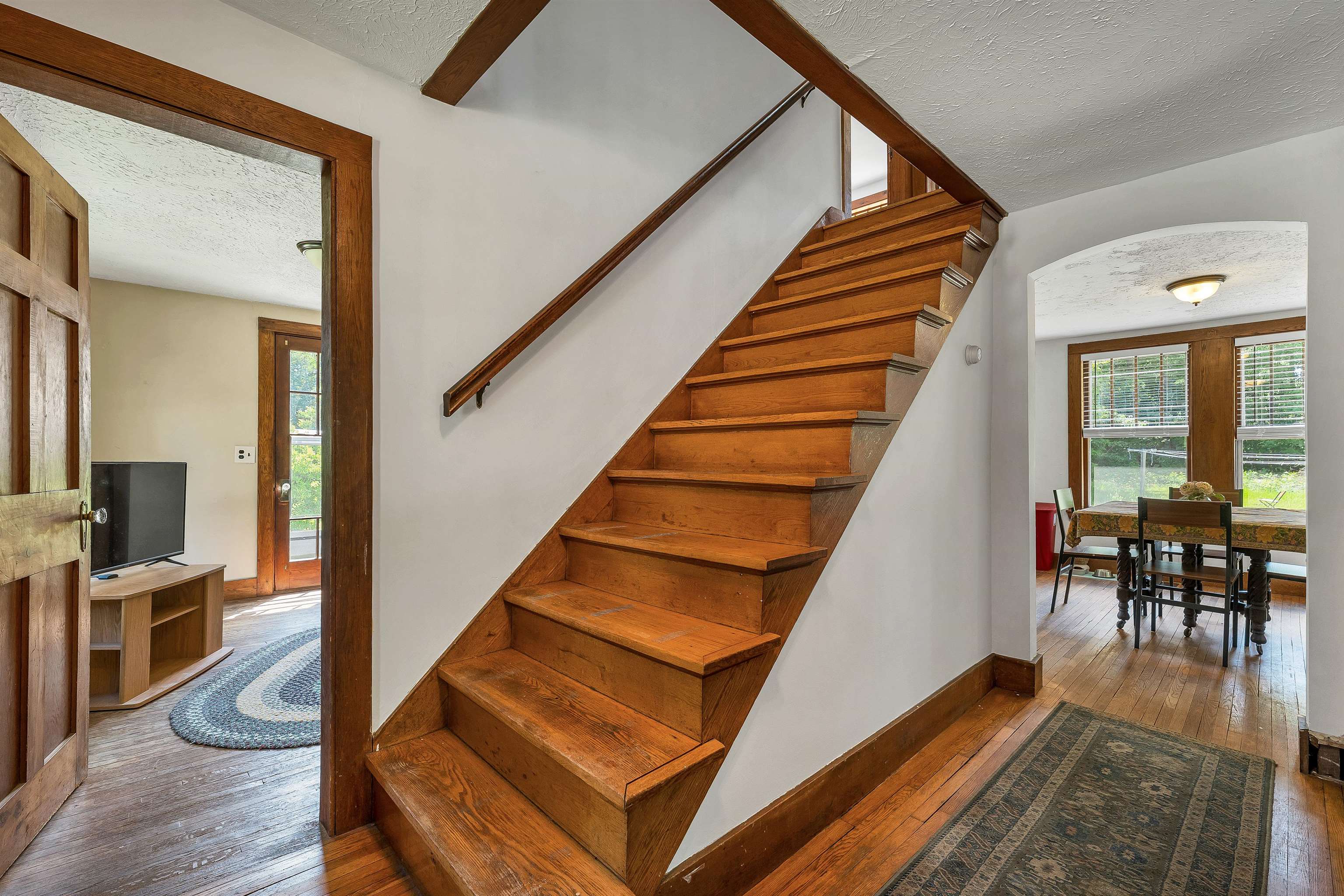 Wooden staircase in an entry hall, with hardwood floors and an adjoining dining room.