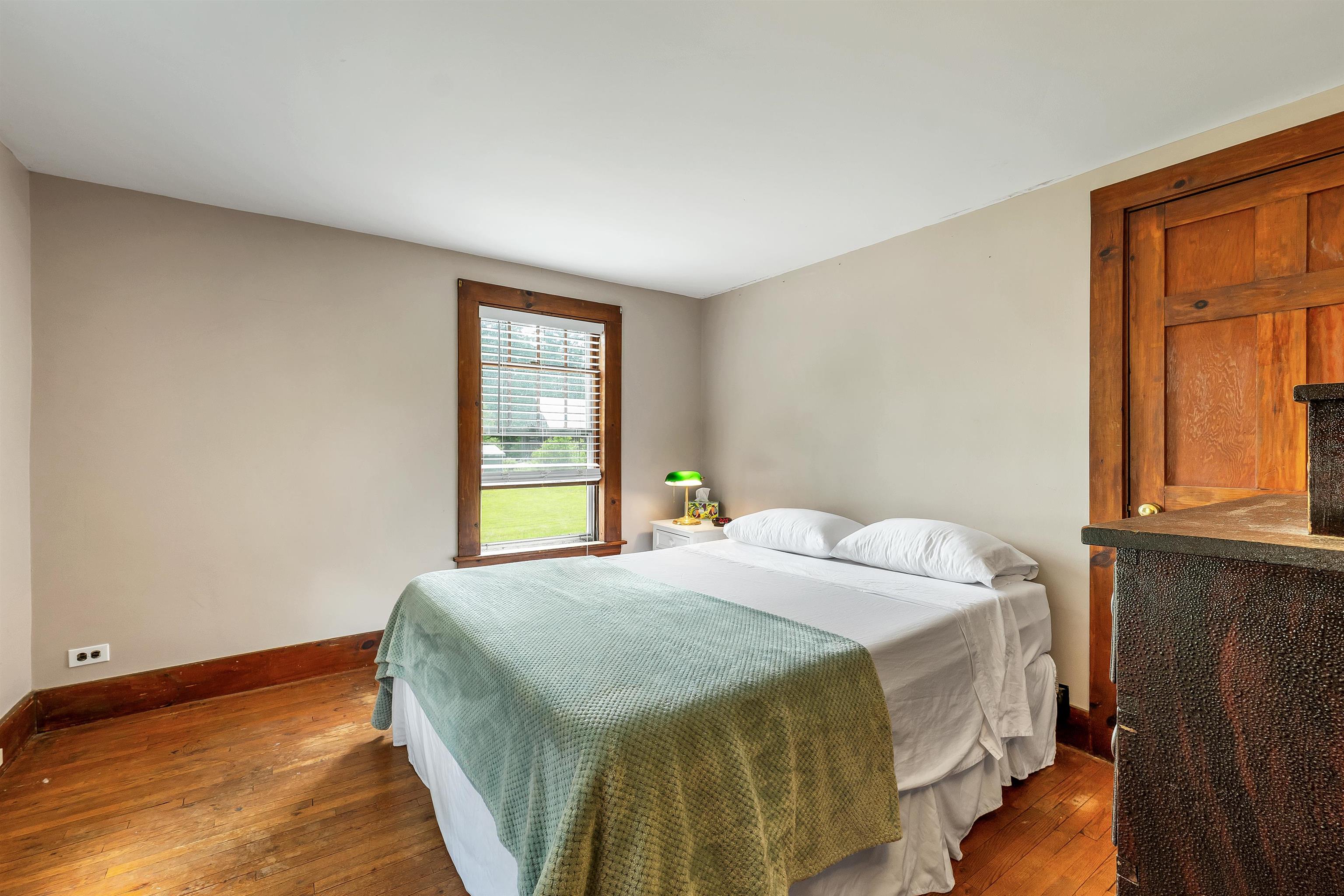 Bedroom with a pale green quilt, wood floors, and a window with blinds.