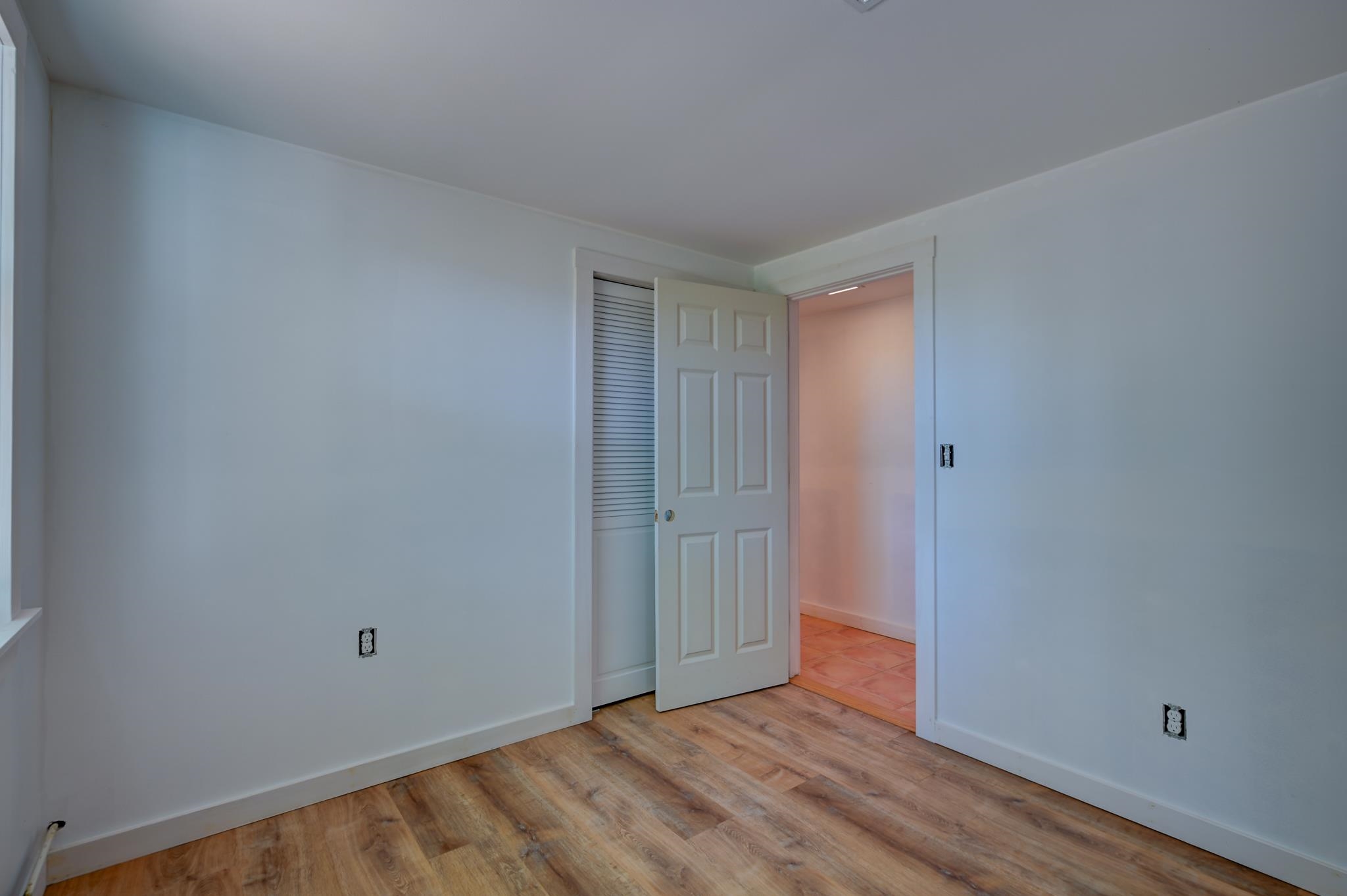 Empty room with wood-look flooring and an open door to a tiled adjoining area.