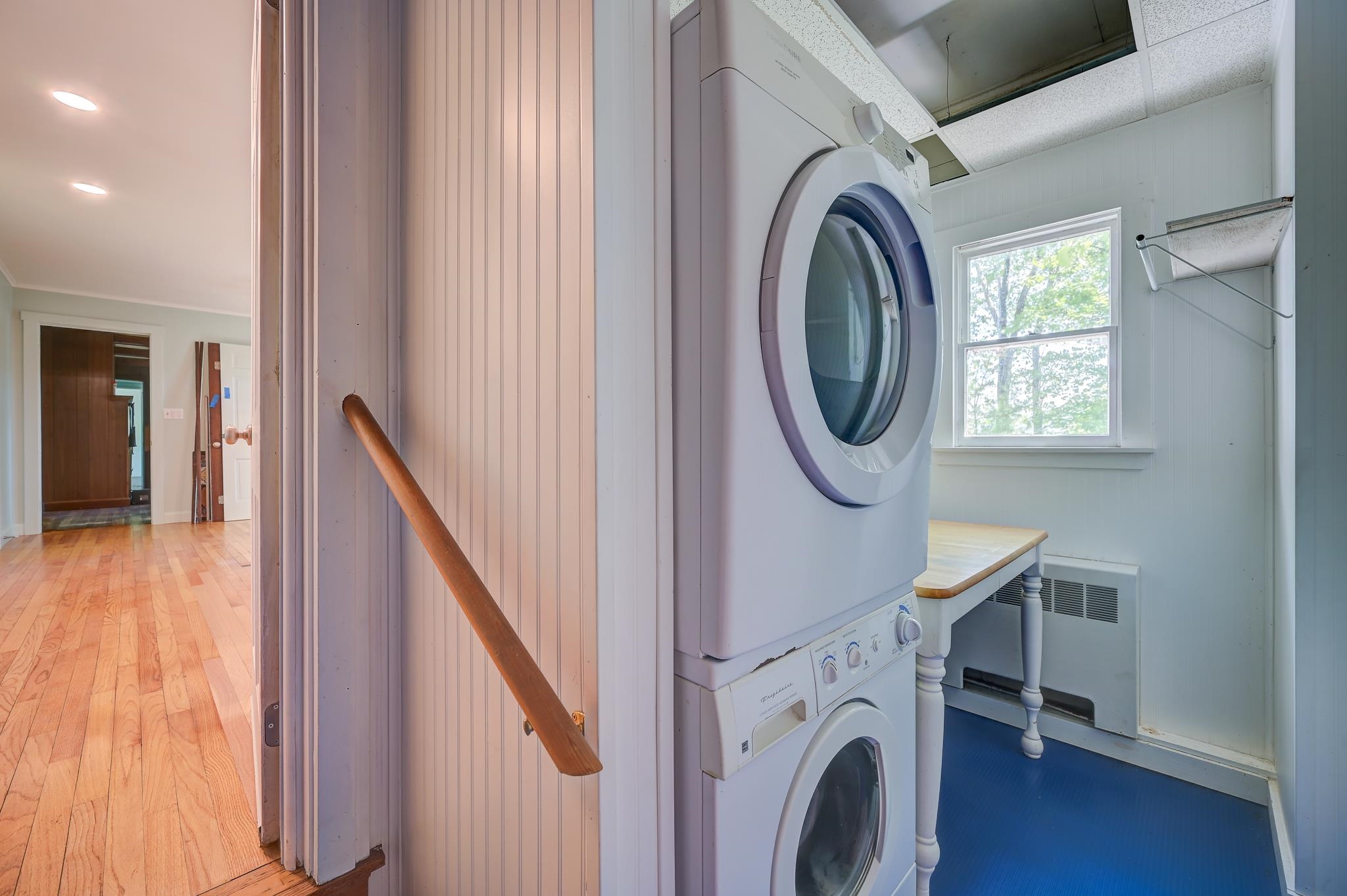 Laundry room with stacked washer and dryer, folding table, and window.