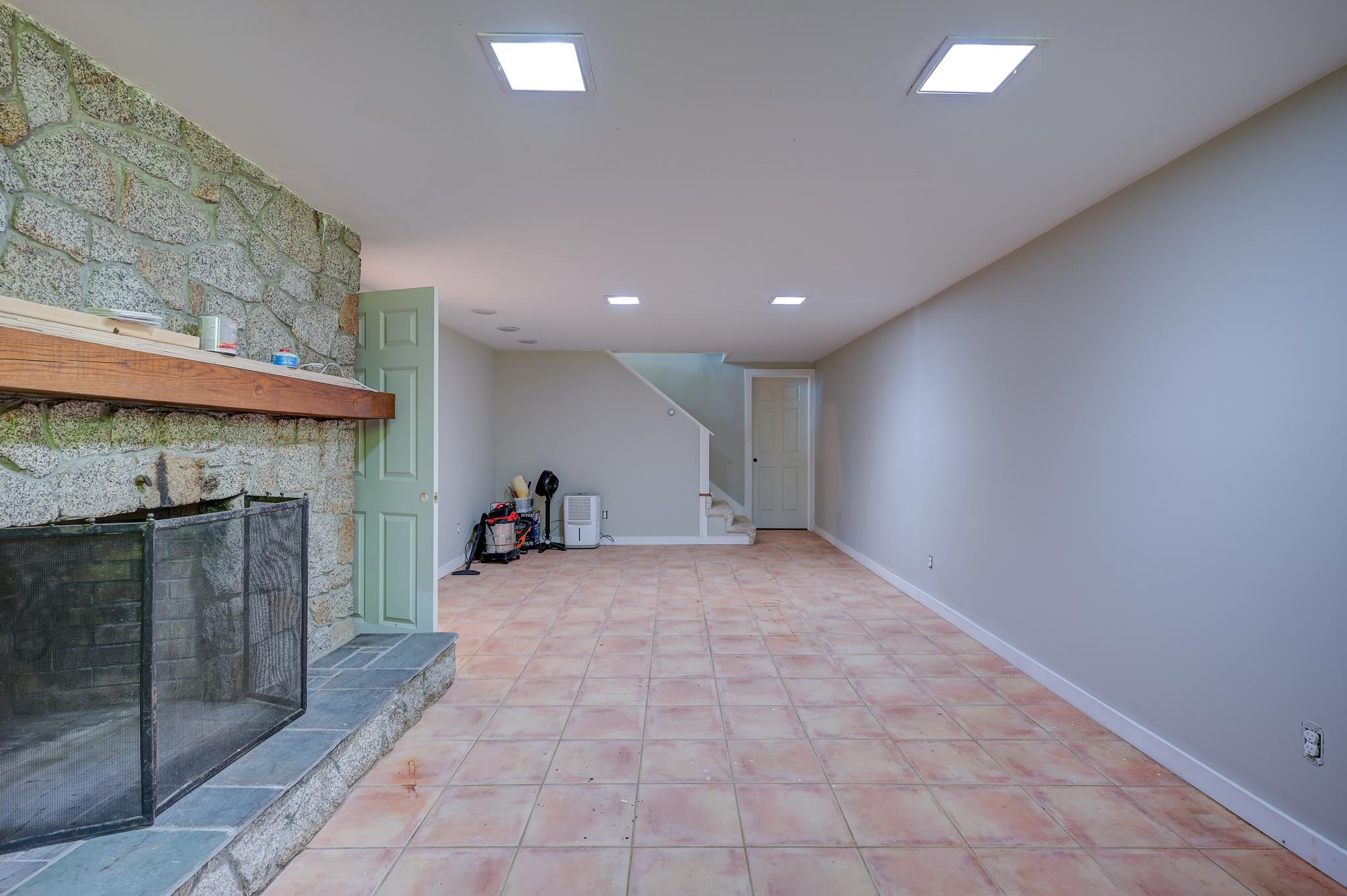 Basement room with a stone fireplace, terracotta tile floor, and stairs.