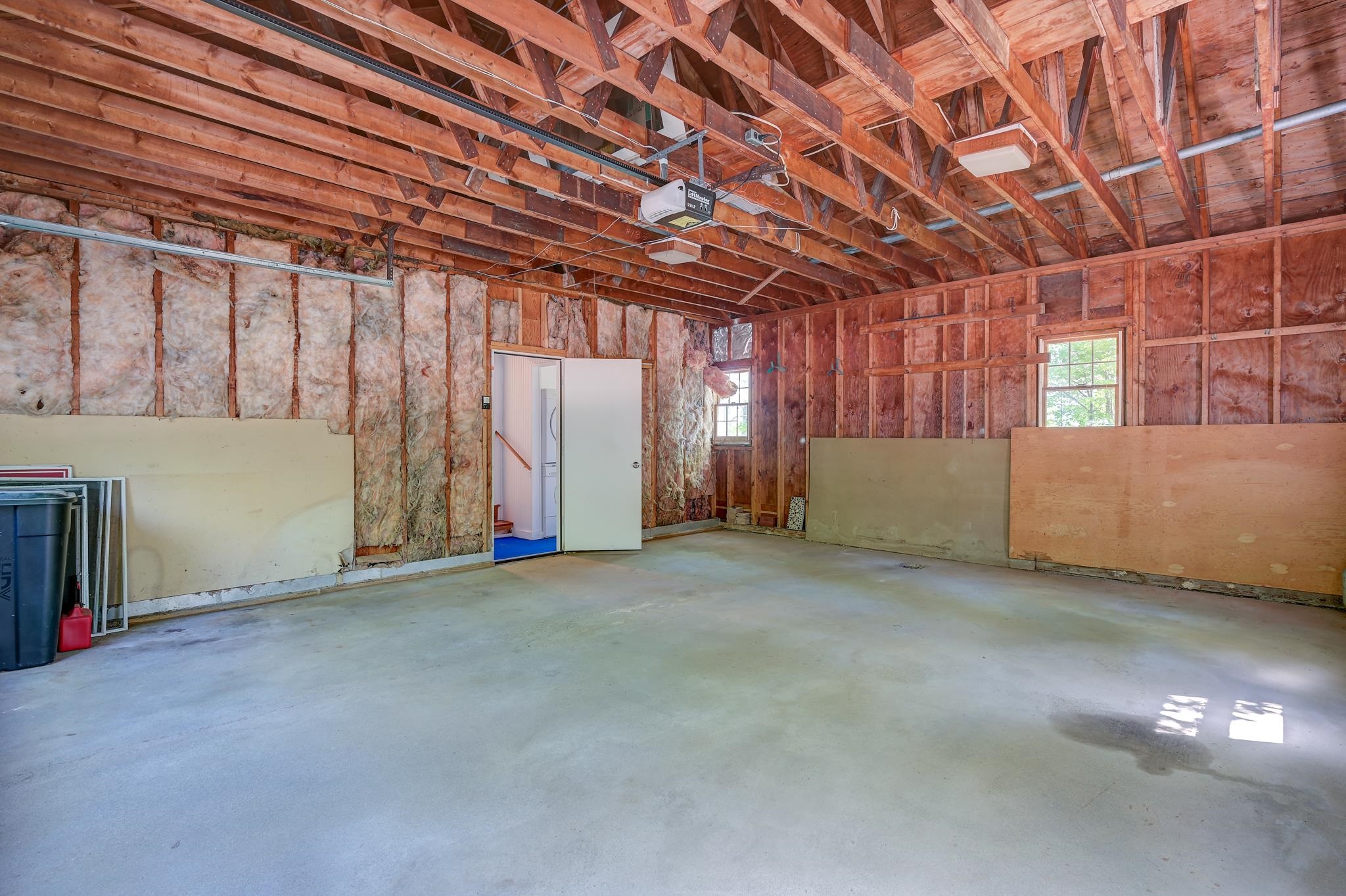 Unfinished garage with exposed roof framing, insulated walls, and a broad concrete floor.