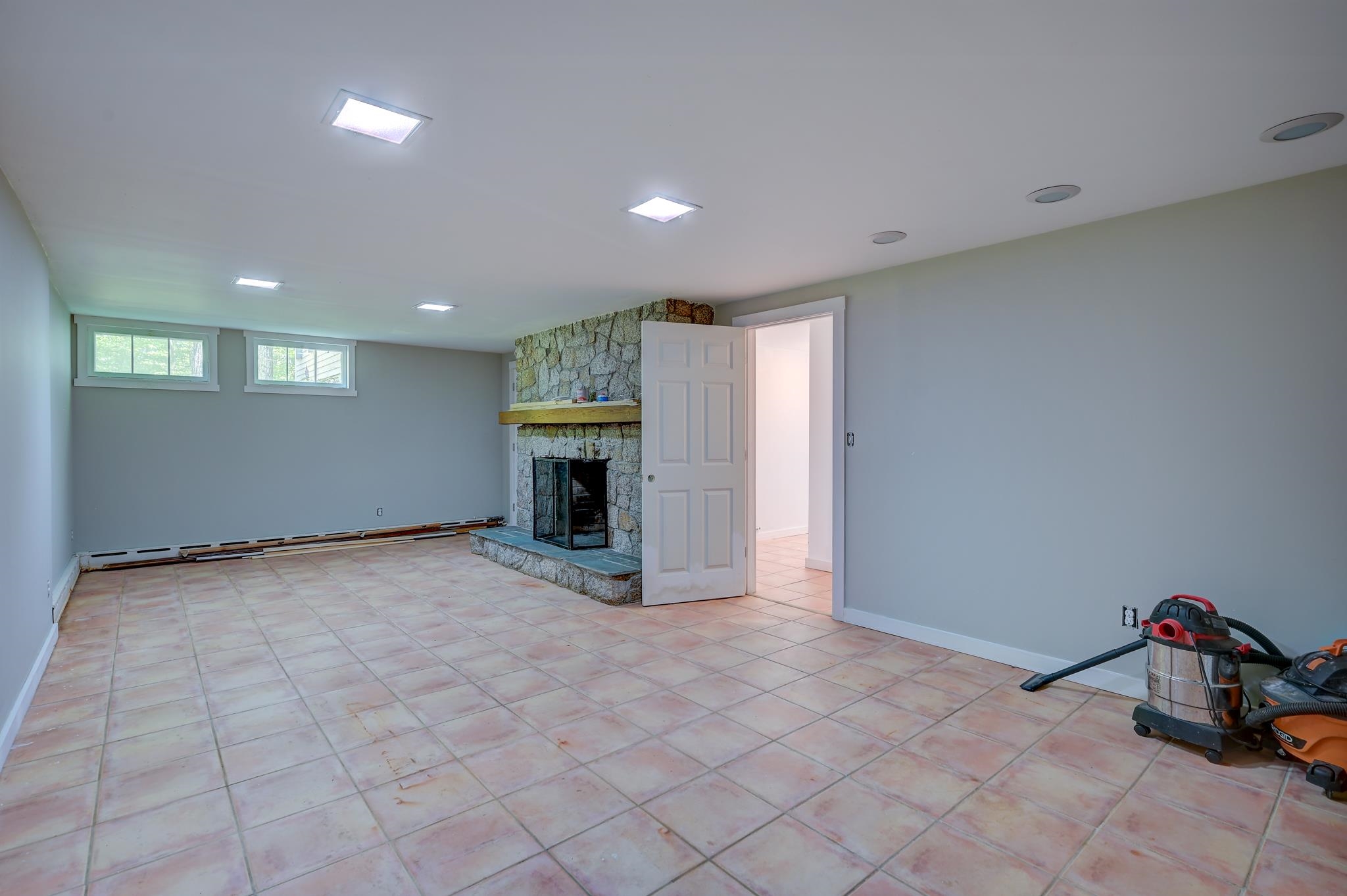 Vacant basement room with tiled floors, a stone fireplace, and small high windows.