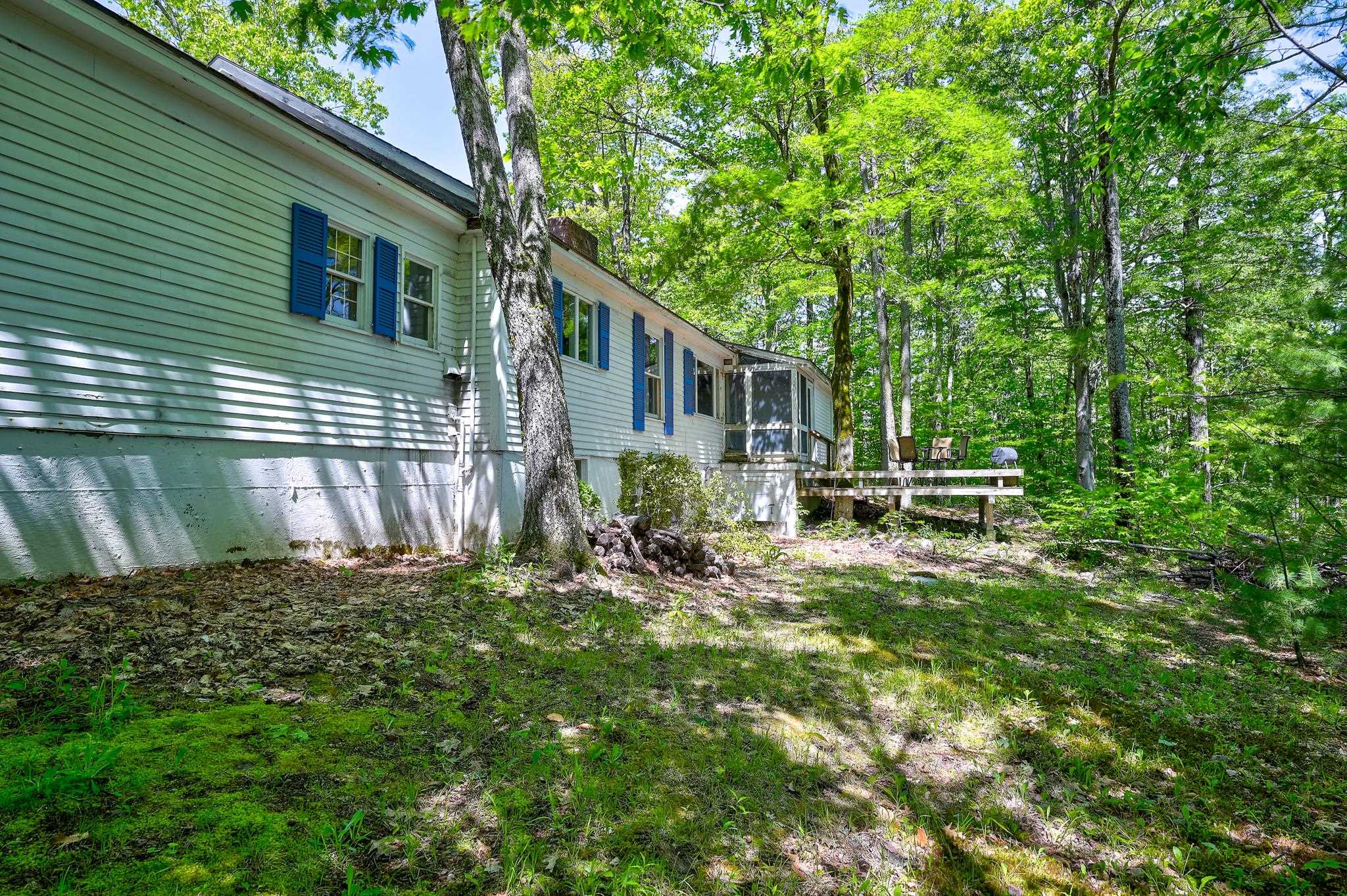 Home with blue shutters and a raised deck, surrounded by trees.