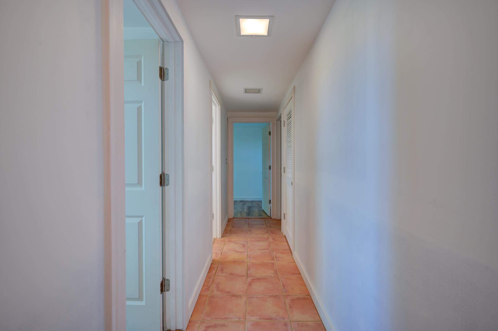Interior hallway with terracotta tile flooring, white walls, and several doorways.