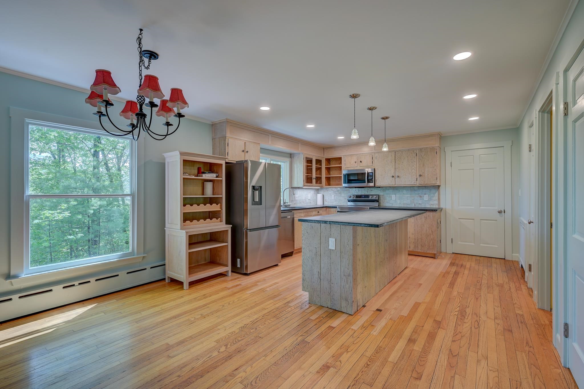 Kitchen with a large island, pale wood cabinetry, stainless steel appliances, and a window overlooking trees.