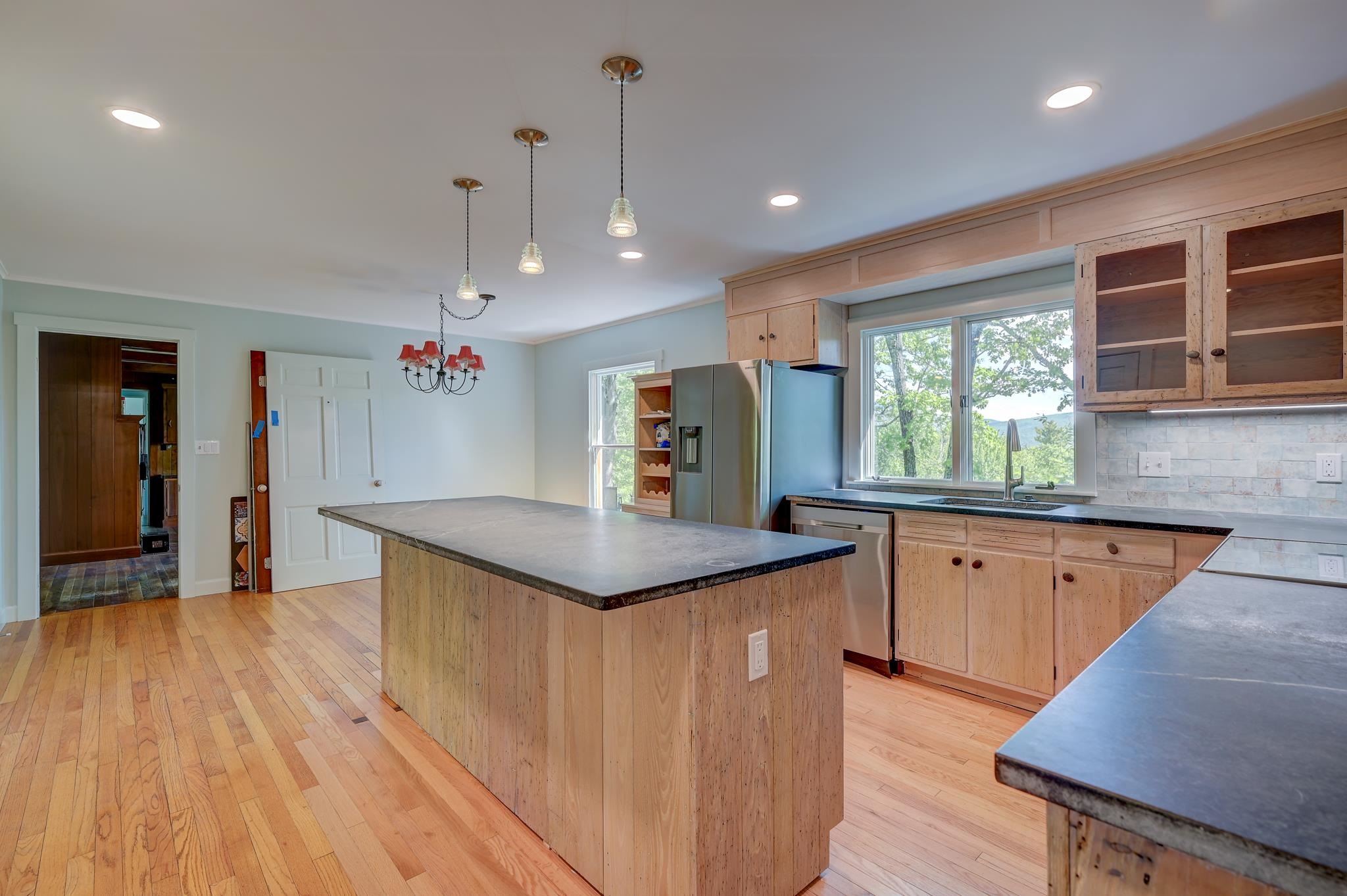Kitchen with light wood cabinets, hardwood floors, a large island, and a wide window above the sink.