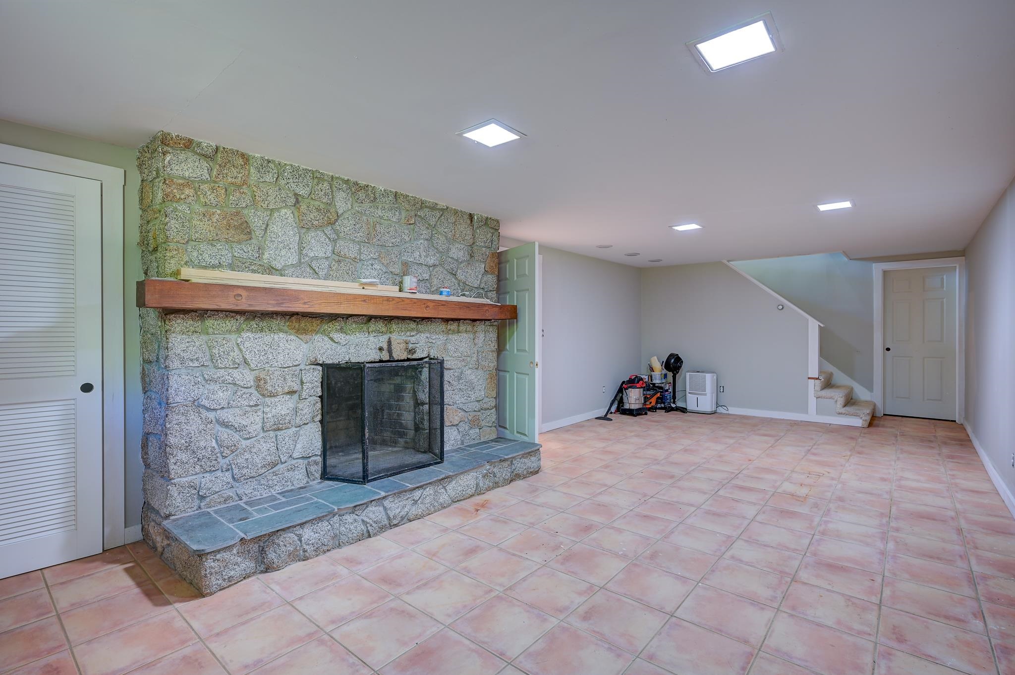 Basement with a large stone fireplace, wooden mantel, pink tile floor, and stairs.