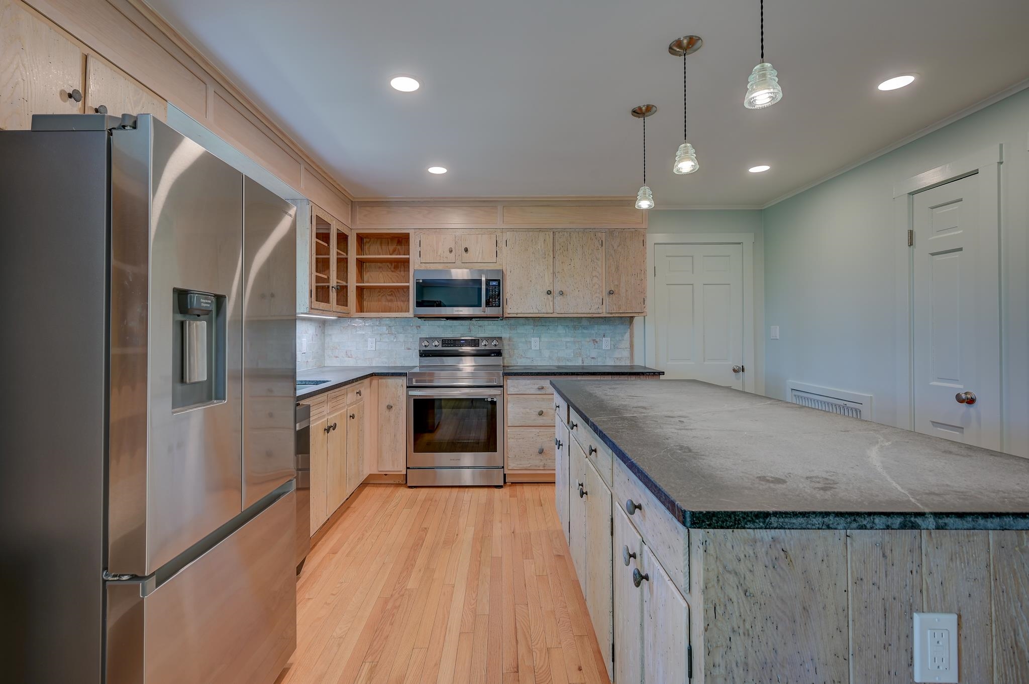 Kitchen with pale wood cabinetry, stainless steel appliances, and a large stone-topped island.