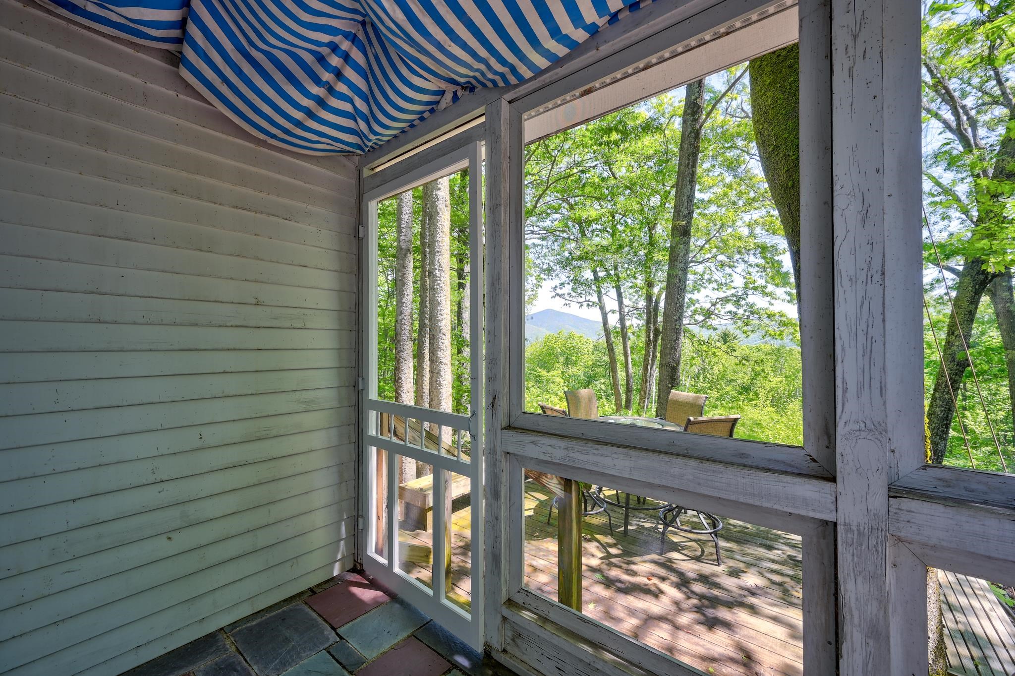 Screened porch with striped awning overlooking a wooded deck and distant mountain.