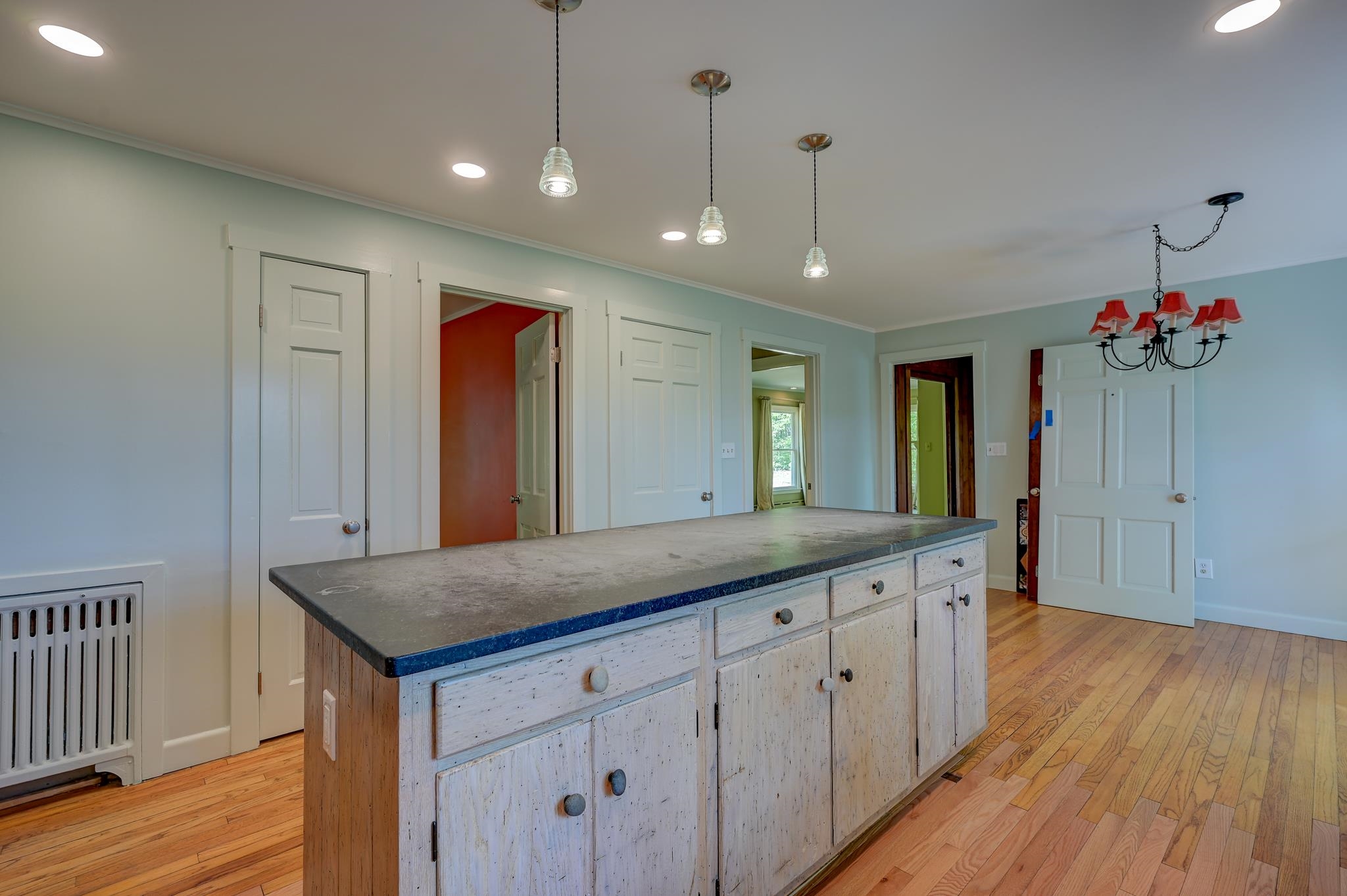 Kitchen with a large distressed white island, dark countertop, hardwood floors, and pendant lights.