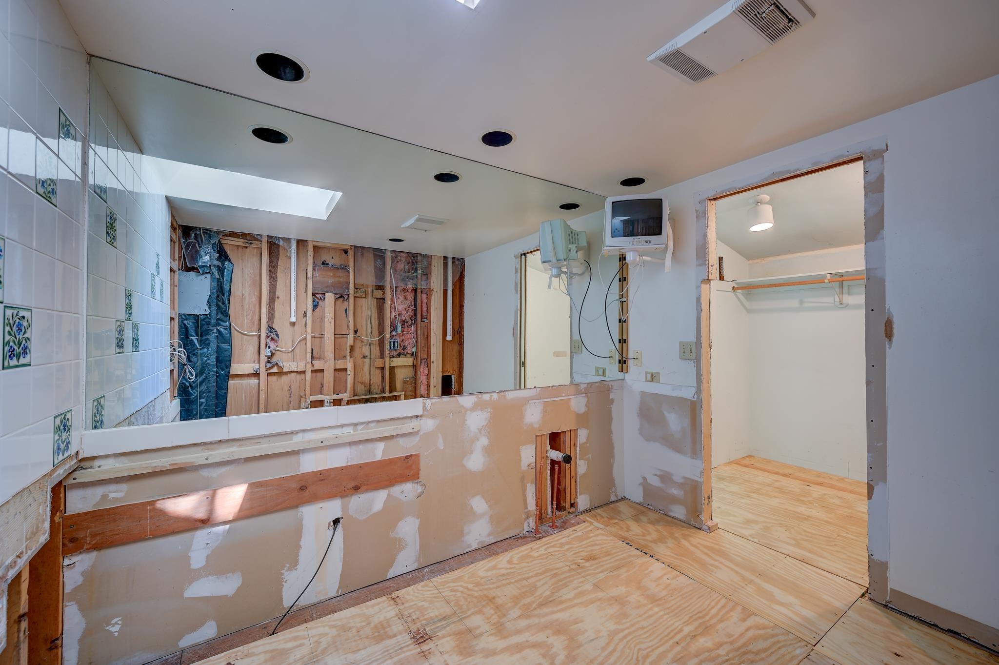 Unfinished bathroom with exposed framing, a tiled wall, and plywood flooring.