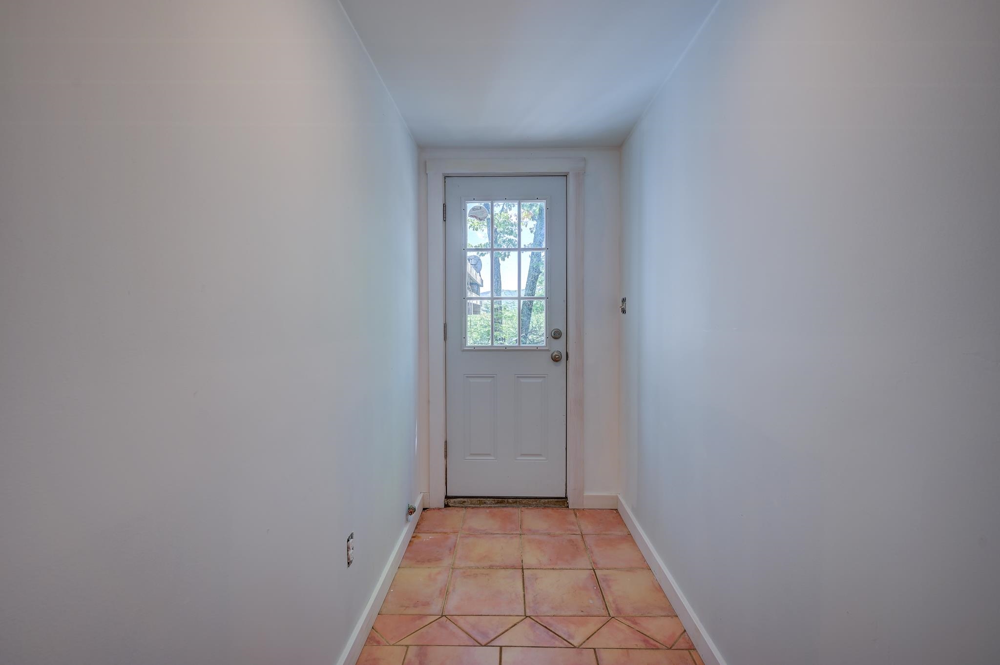 Unfurnished entry hall with terracotta tile flooring and a white glass-paneled door.