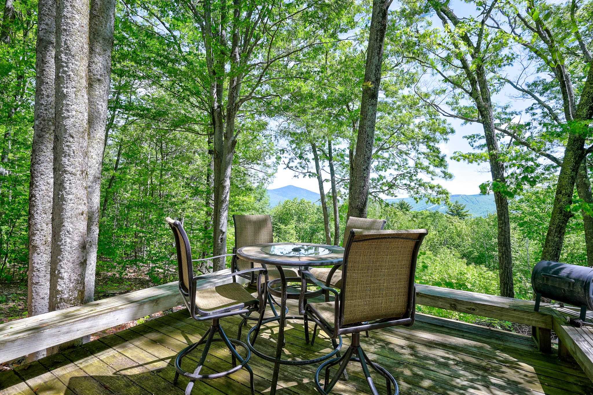 Wooden deck with outdoor dining set and mountain views through leafy trees.