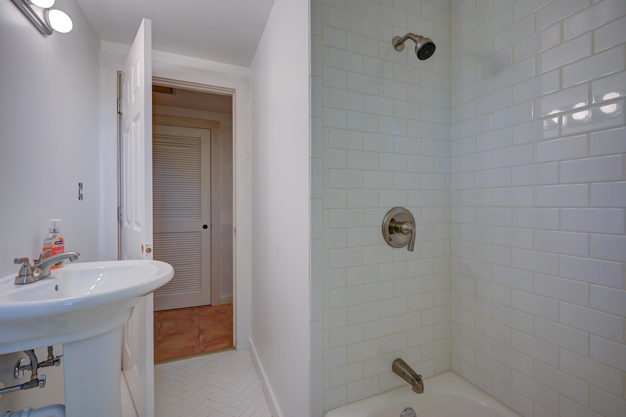 Bathroom with white subway-tile shower surround, bathtub, pedestal sink, and open doorway.