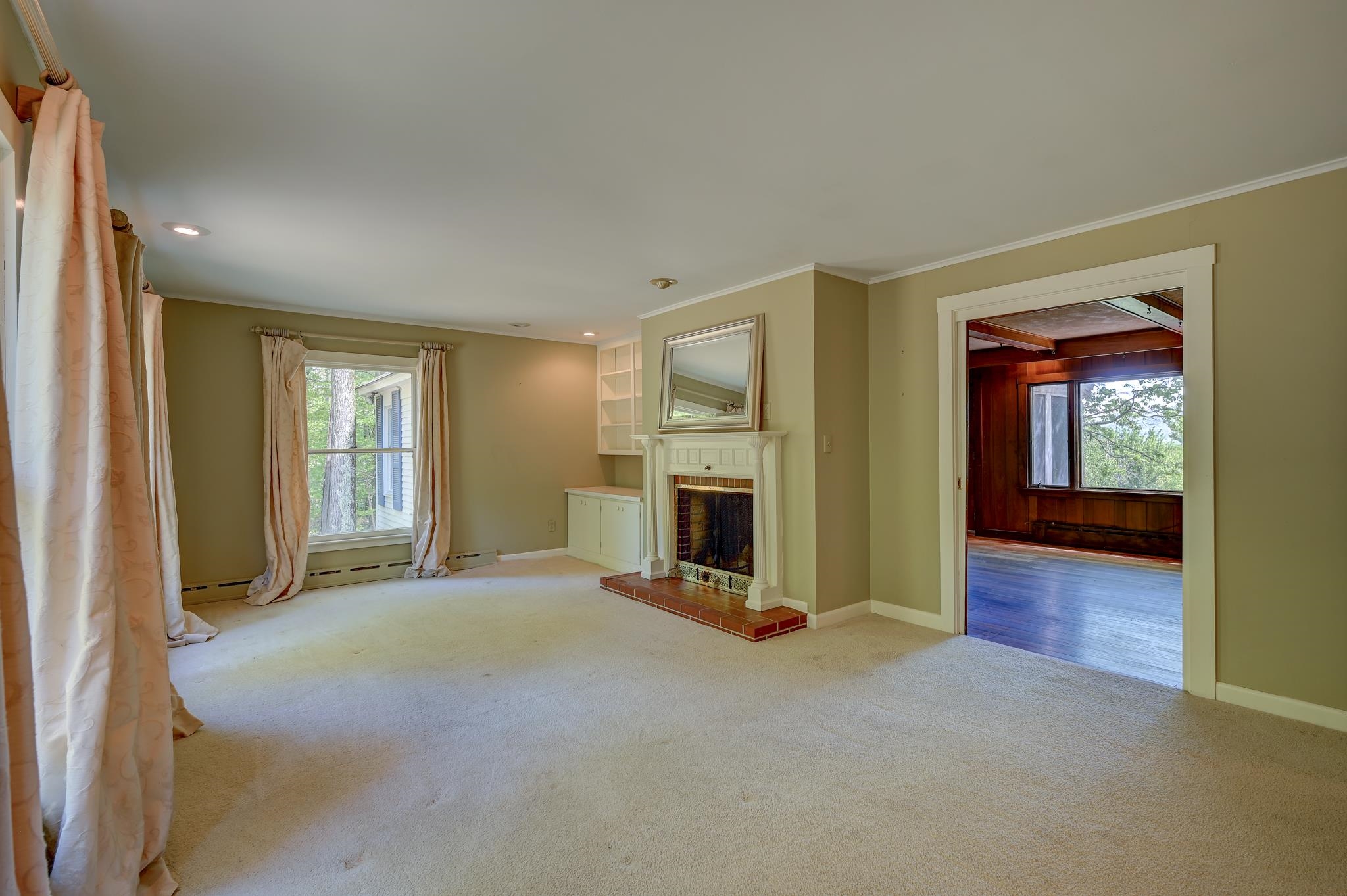 Empty living room with a white fireplace and doorway to a wood-paneled room.