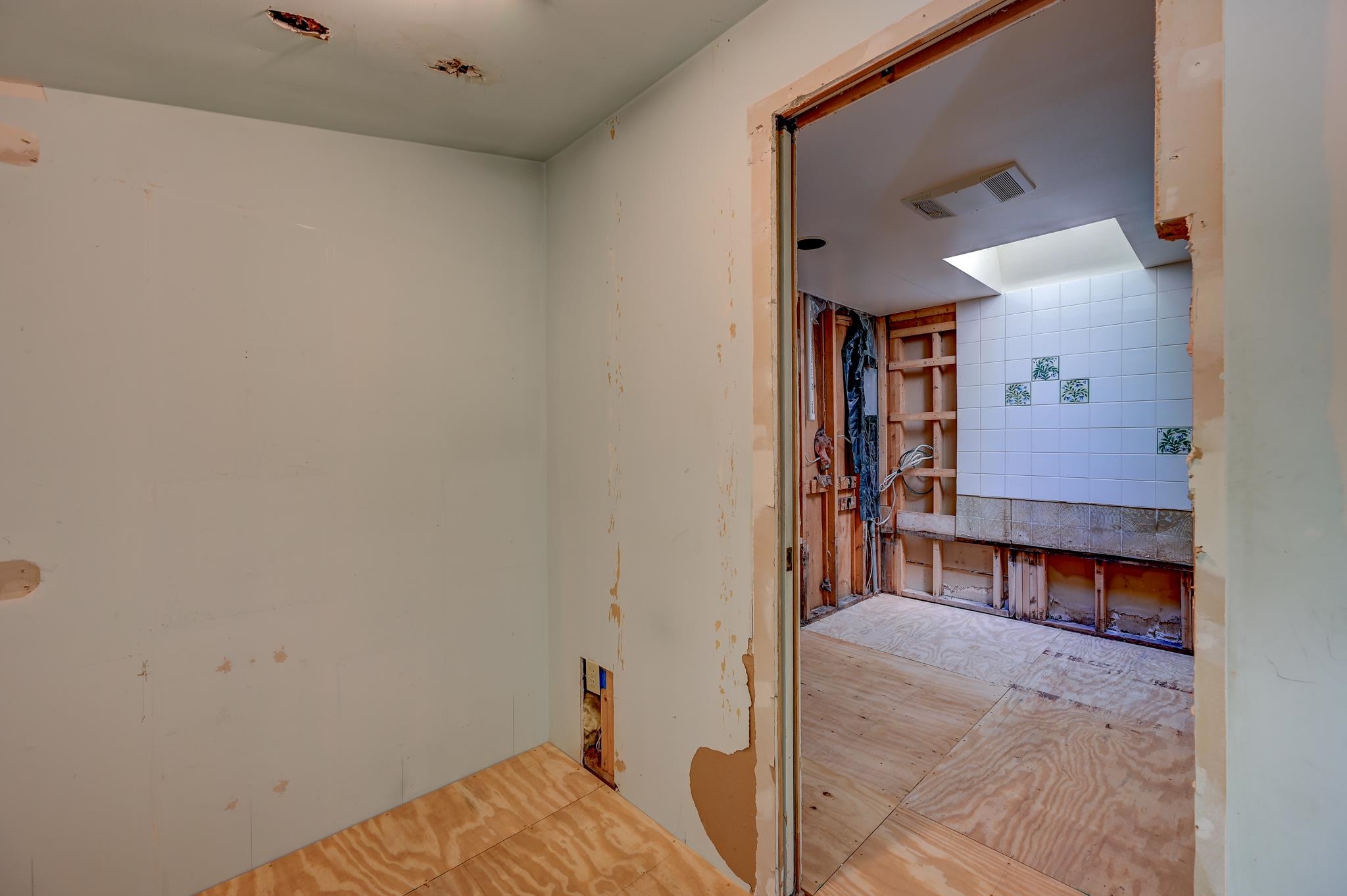 Bathroom under renovation with exposed framing, white decorative tile, and plywood floors.