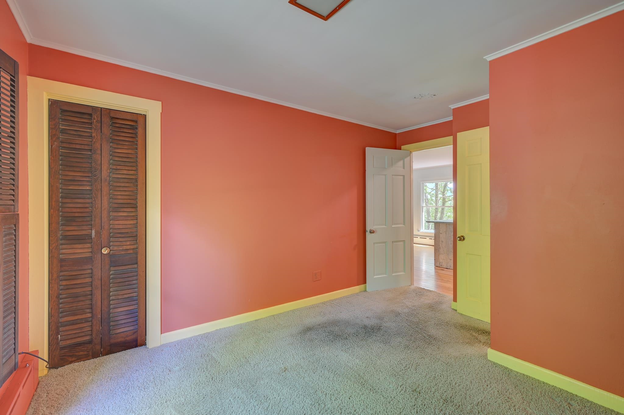 Empty bedroom with coral walls, yellow trim, carpet, and dark louvered closet doors.