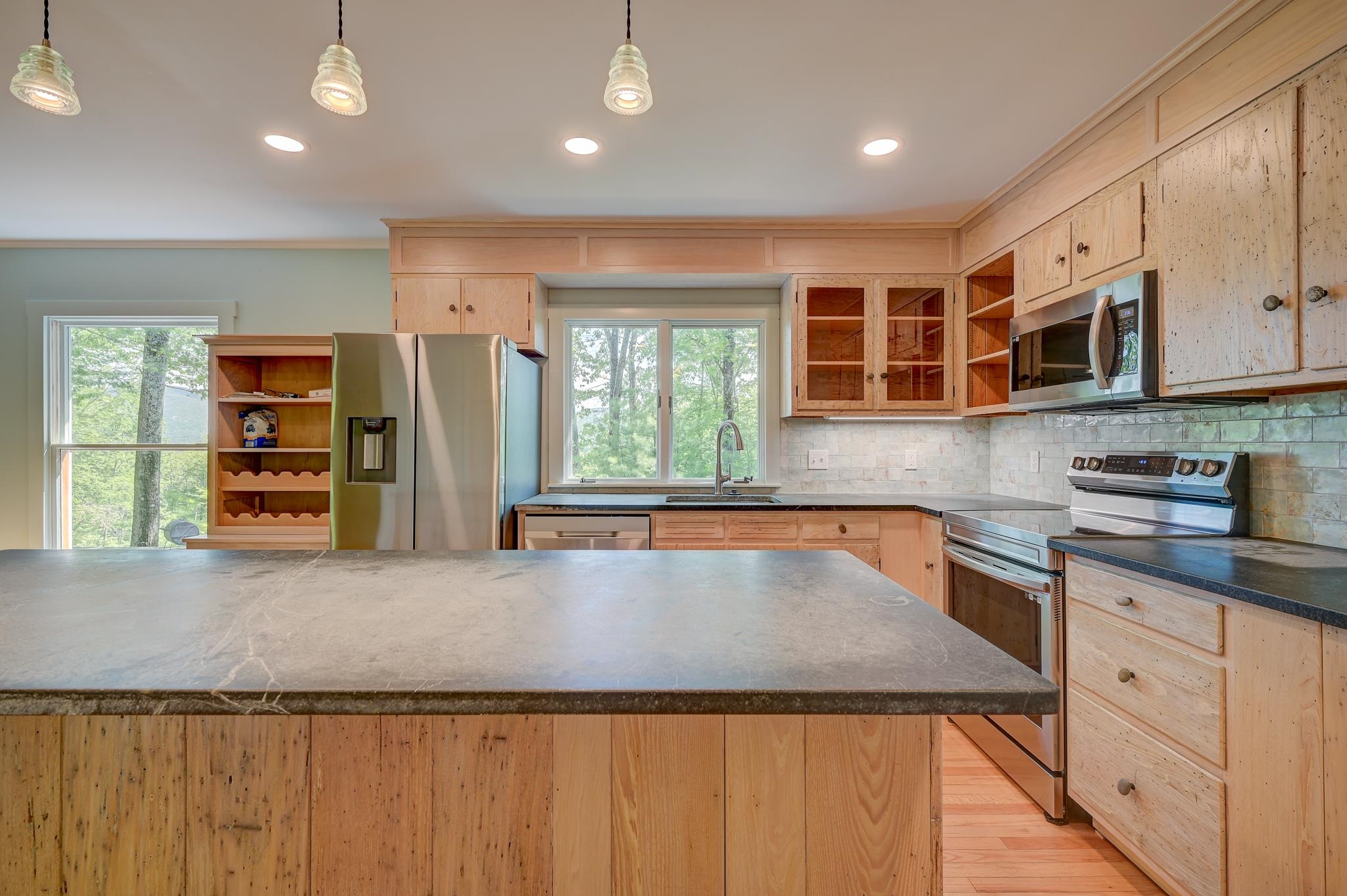 Kitchen with wood cabinetry, a large stone island, stainless appliances, and leafy views through the windows.