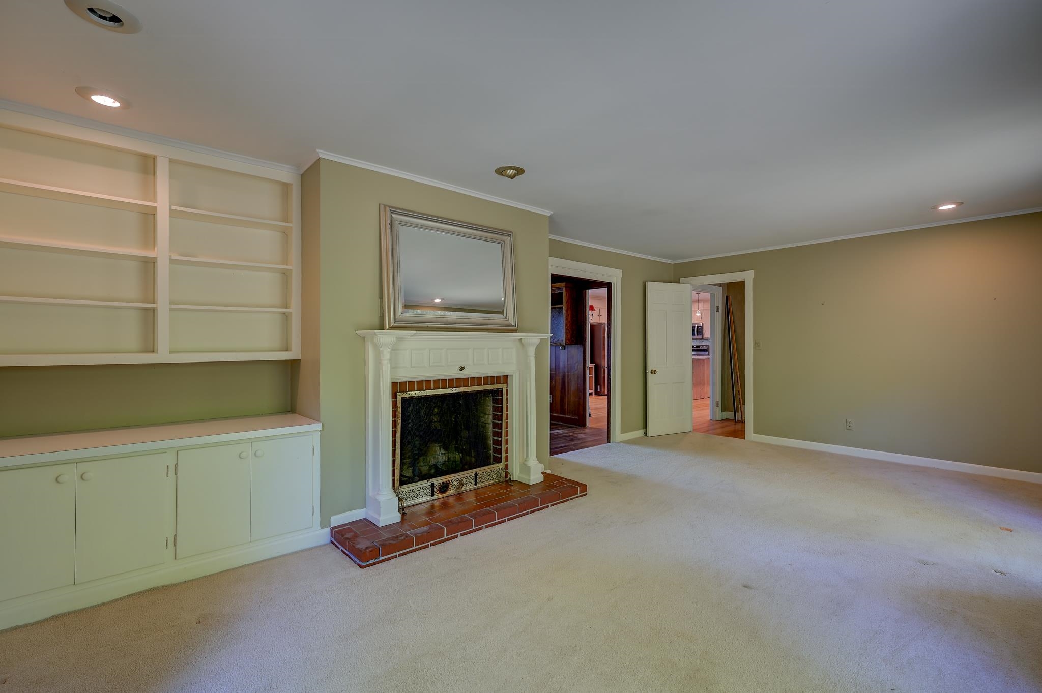 Vacant living room with built-in shelves and a white fireplace with brick hearth.