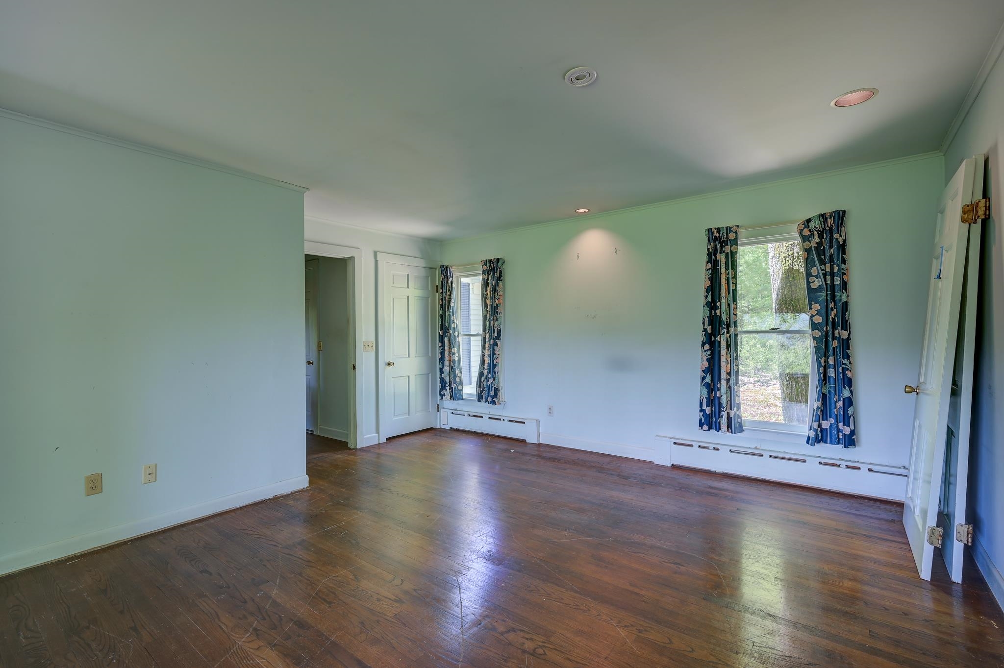 Unfurnished bedroom with dark hardwood floors and two curtained windows.