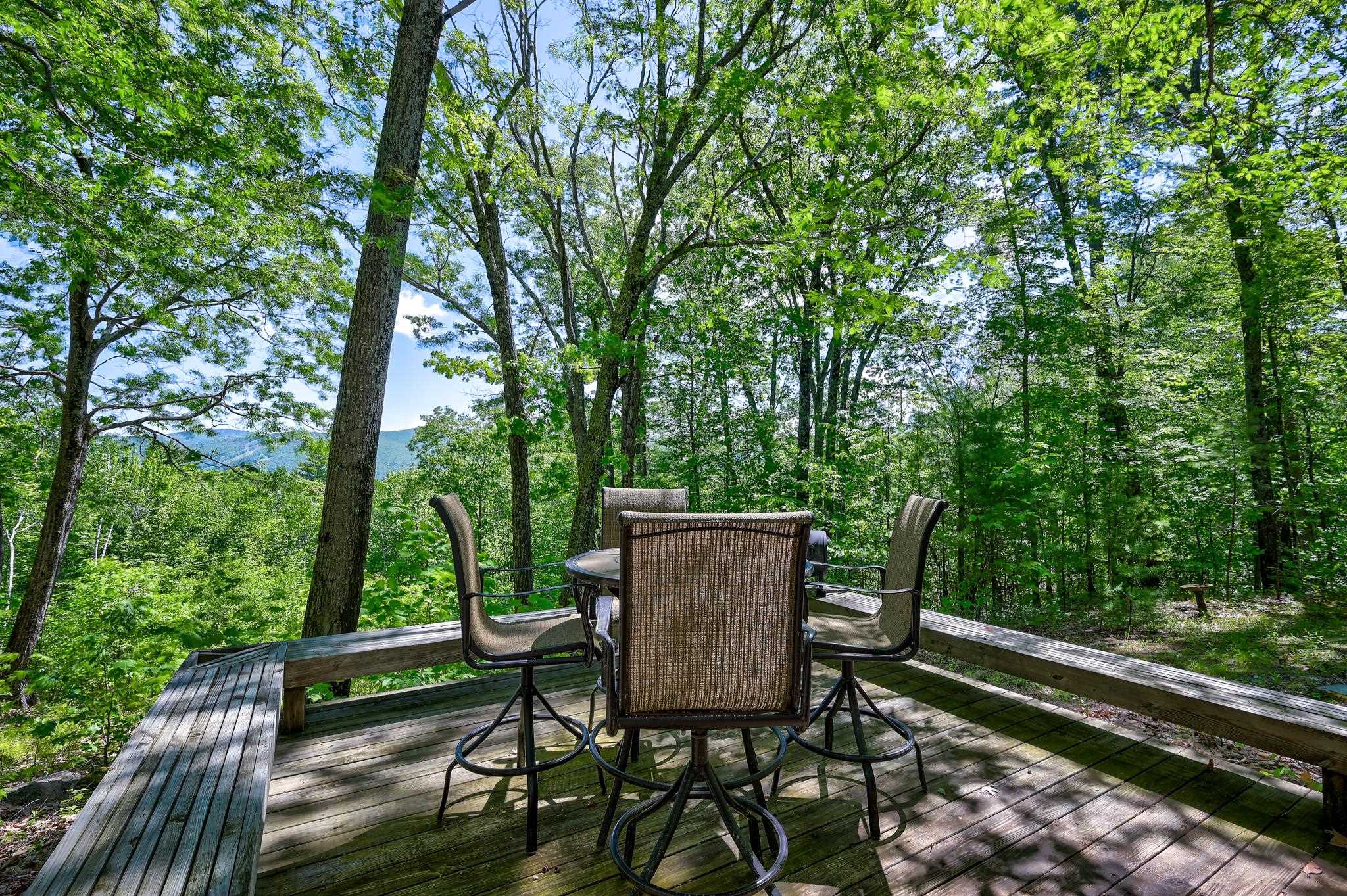 Furnished wooden deck surrounded by trees, with a distant mountain view.