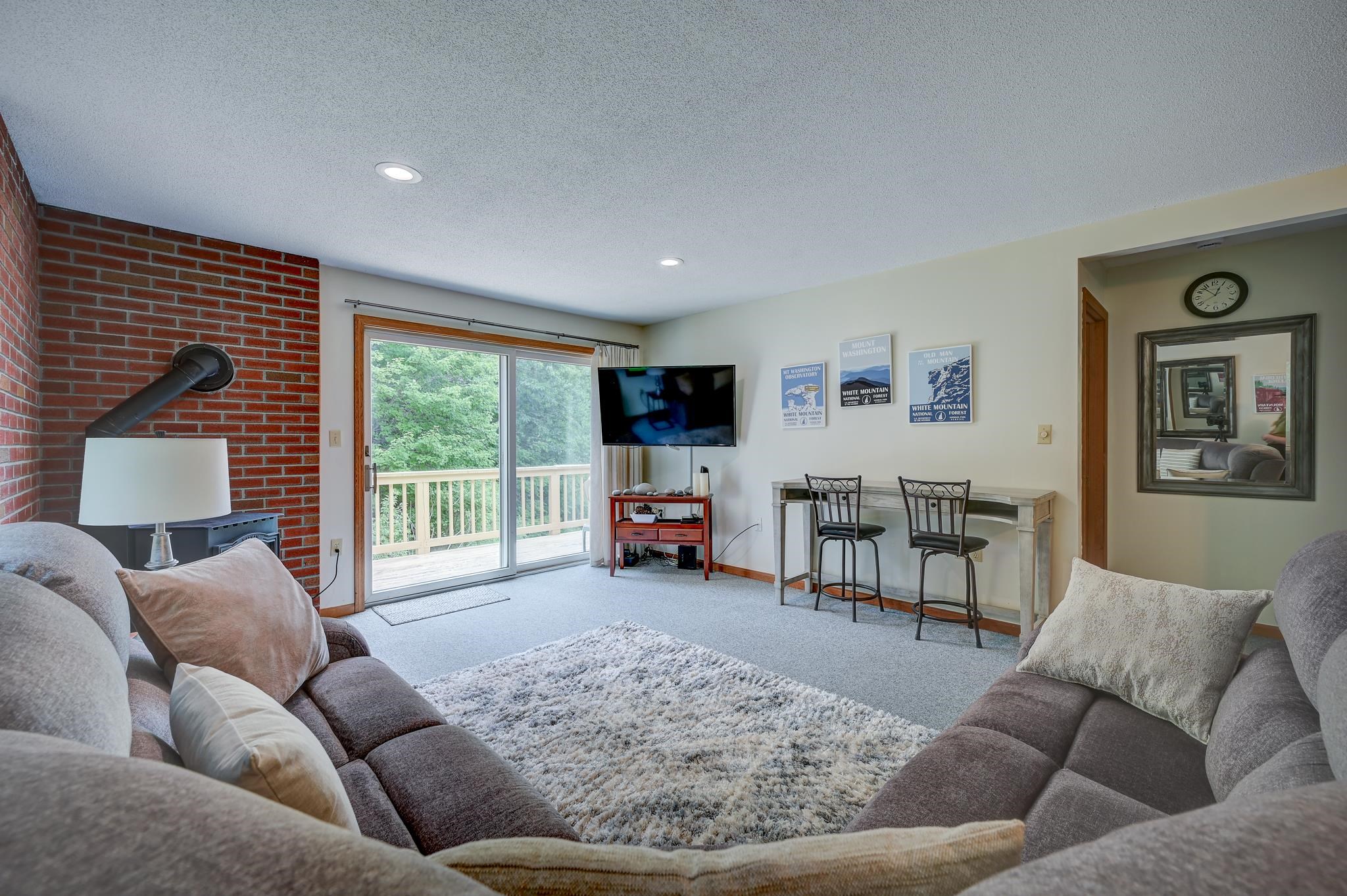 Living room with gray sofas, brick fireplace wall, and sliding doors to a tree-lined deck.