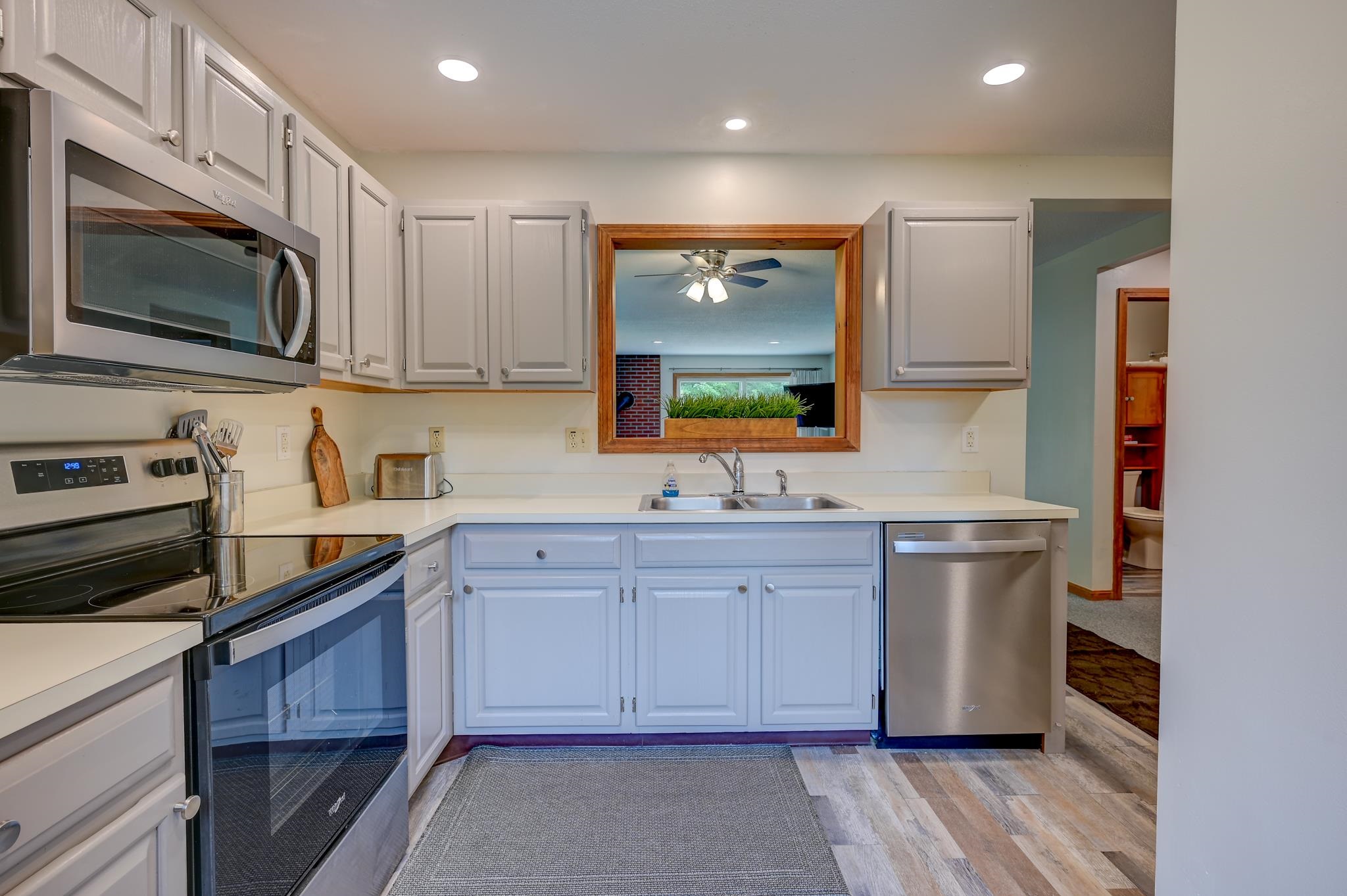 Kitchen with white cabinets, stainless steel appliances, and a wood-trimmed pass-through window above the sink.