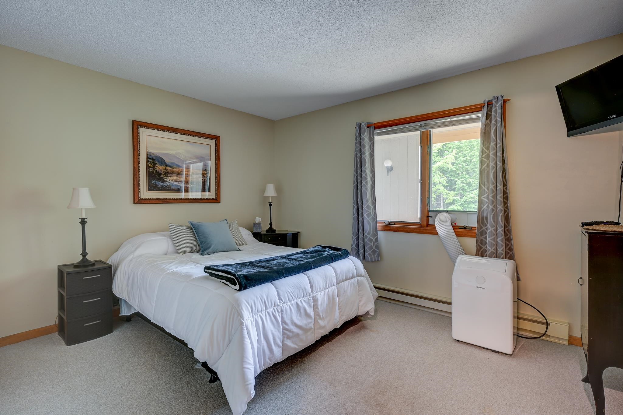Furnished bedroom with a white bed, blue accents, and a window overlooking trees.