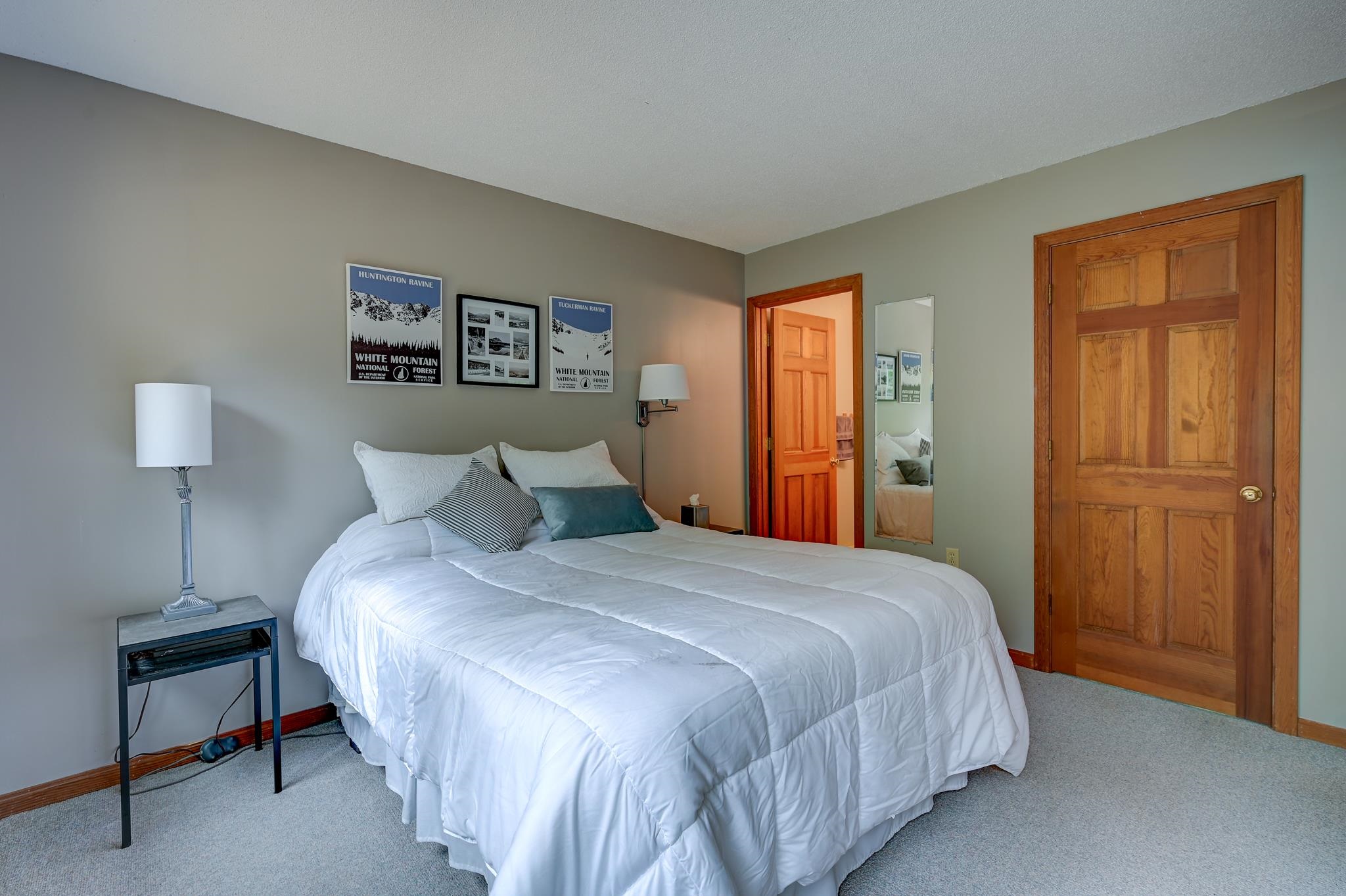 Bedroom with a white-covered bed, framed mountain posters, and warm wood doors.