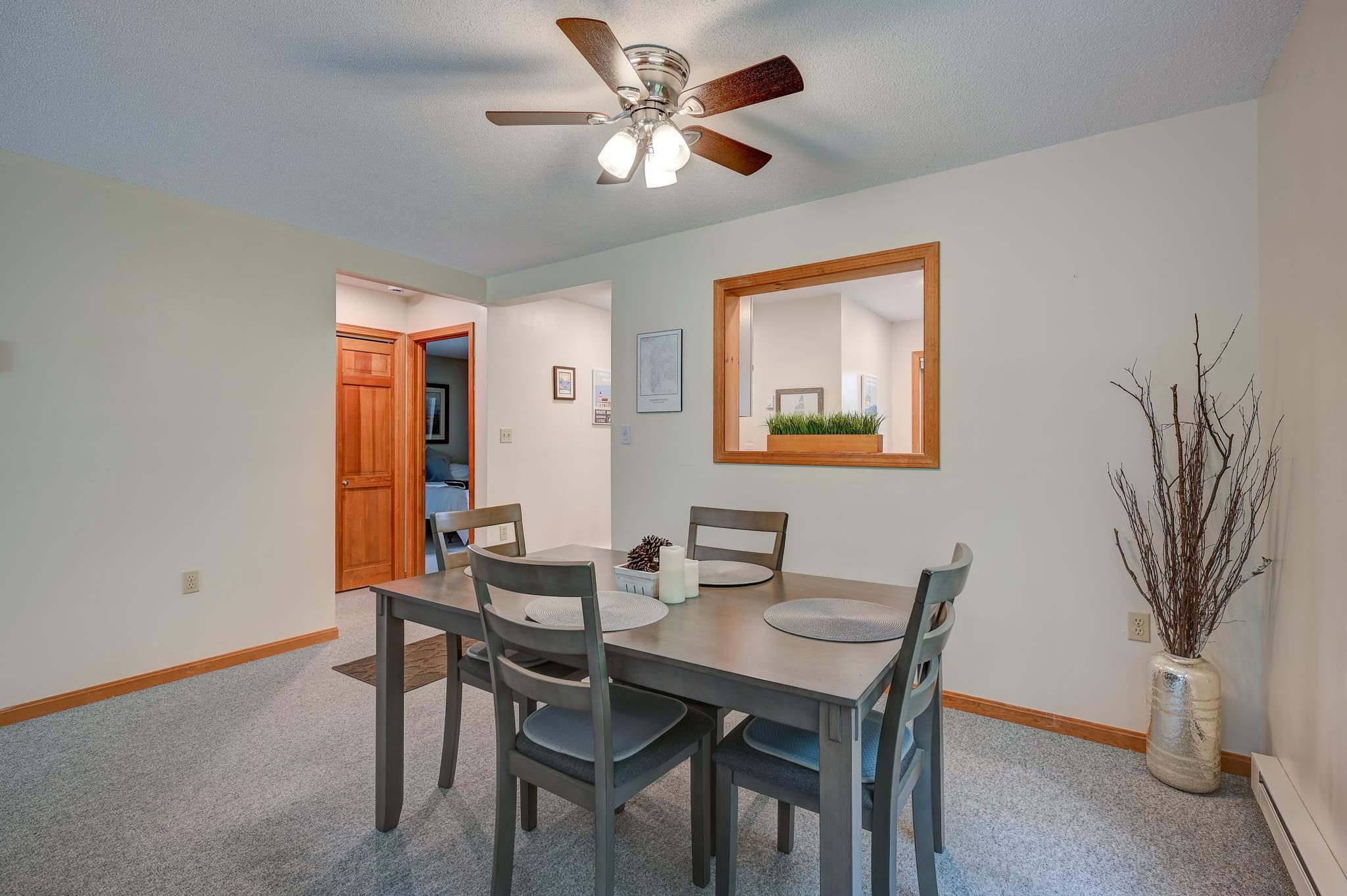 Dining room with gray table and chairs, ceiling fan, and wood-trimmed pass-through window.