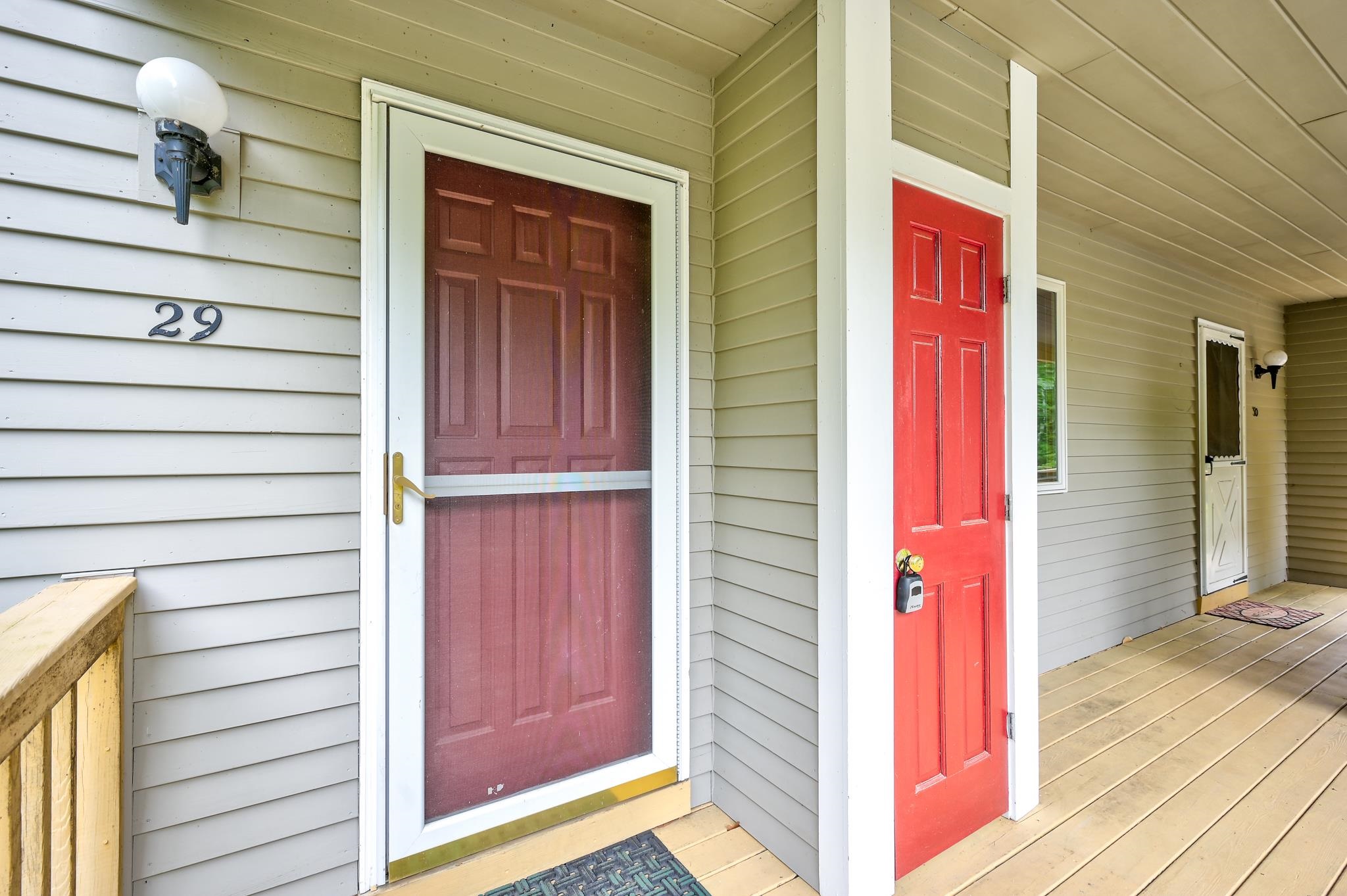 Unit 29’s covered porch entrance with a screened storm door beside a bright red neighboring door.