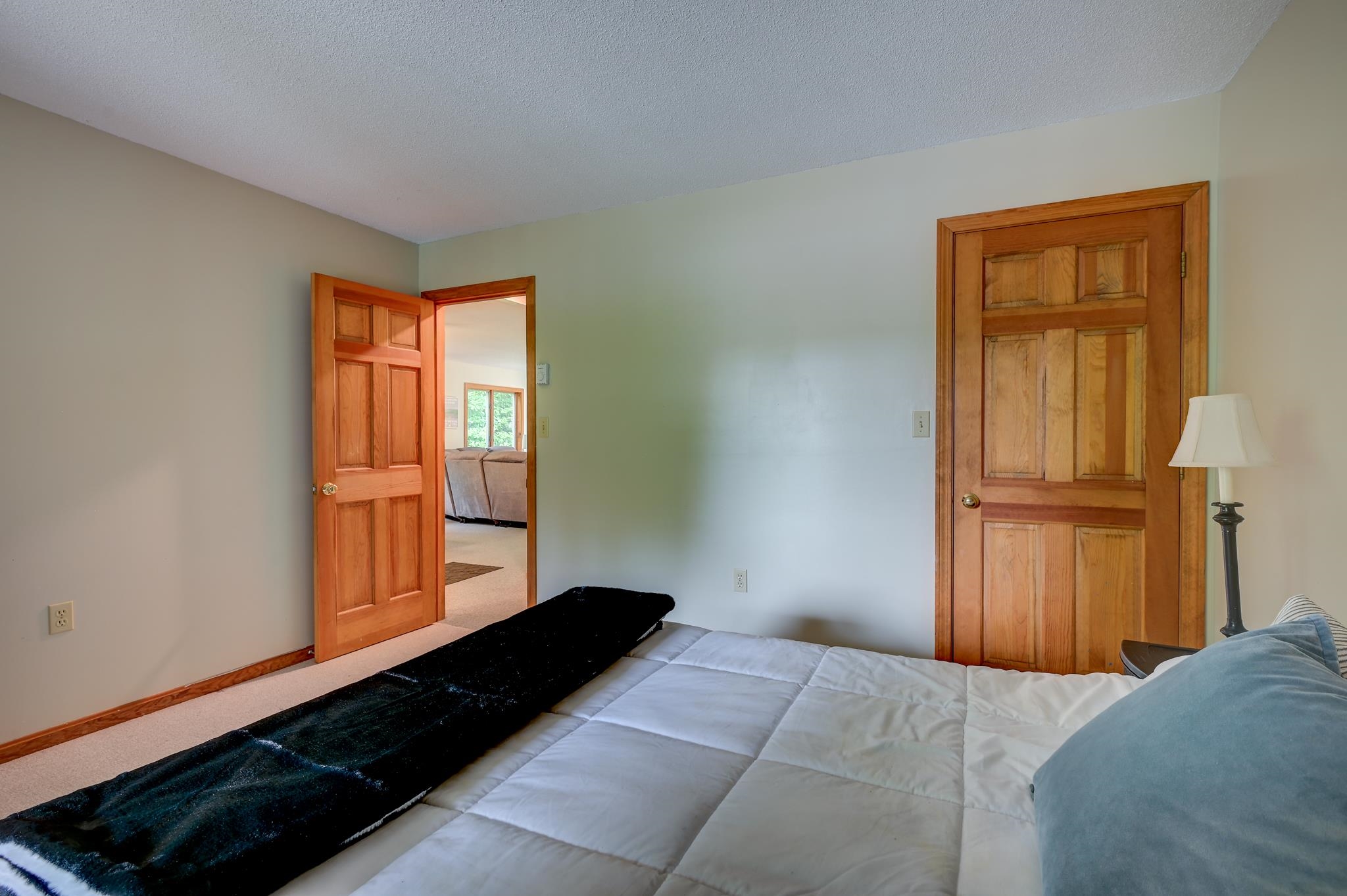 Bedroom with white quilted bed, dark throw, and open wooden doorway to a sitting room.