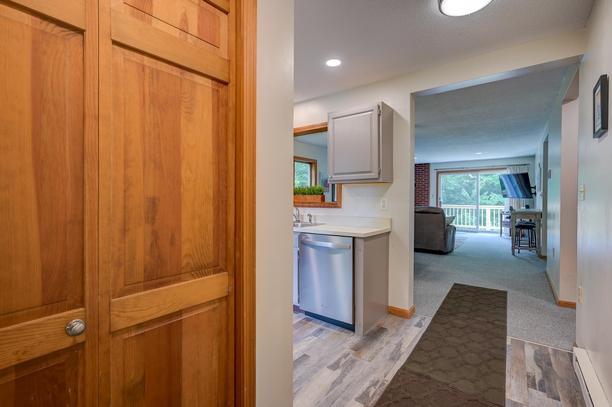 Condo entry looking past a compact kitchen toward a carpeted living room and balcony.